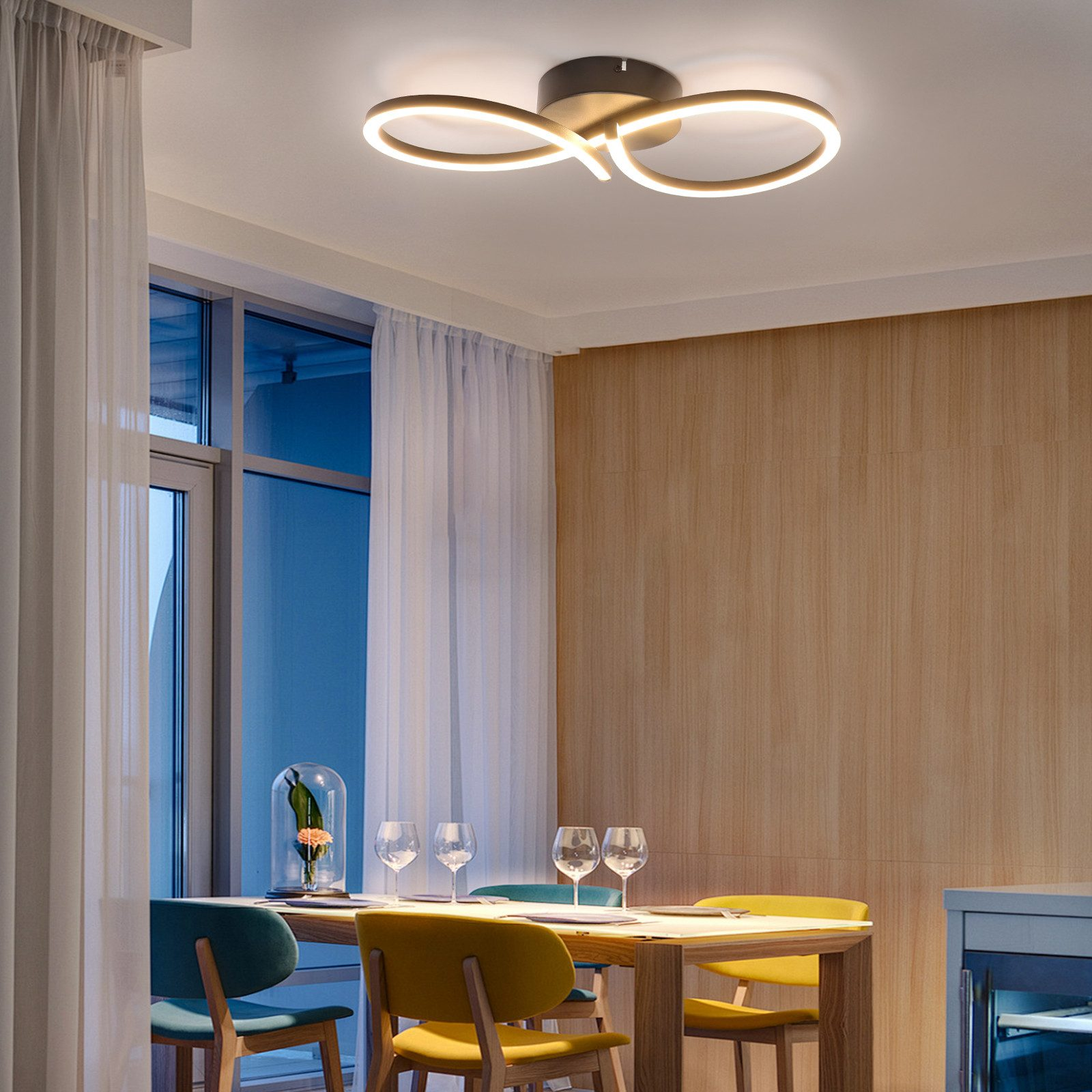 Lampada da soffitto con design a simbolo di infinito. La luce è bianca. La stanza comprende tavolo e sedie.