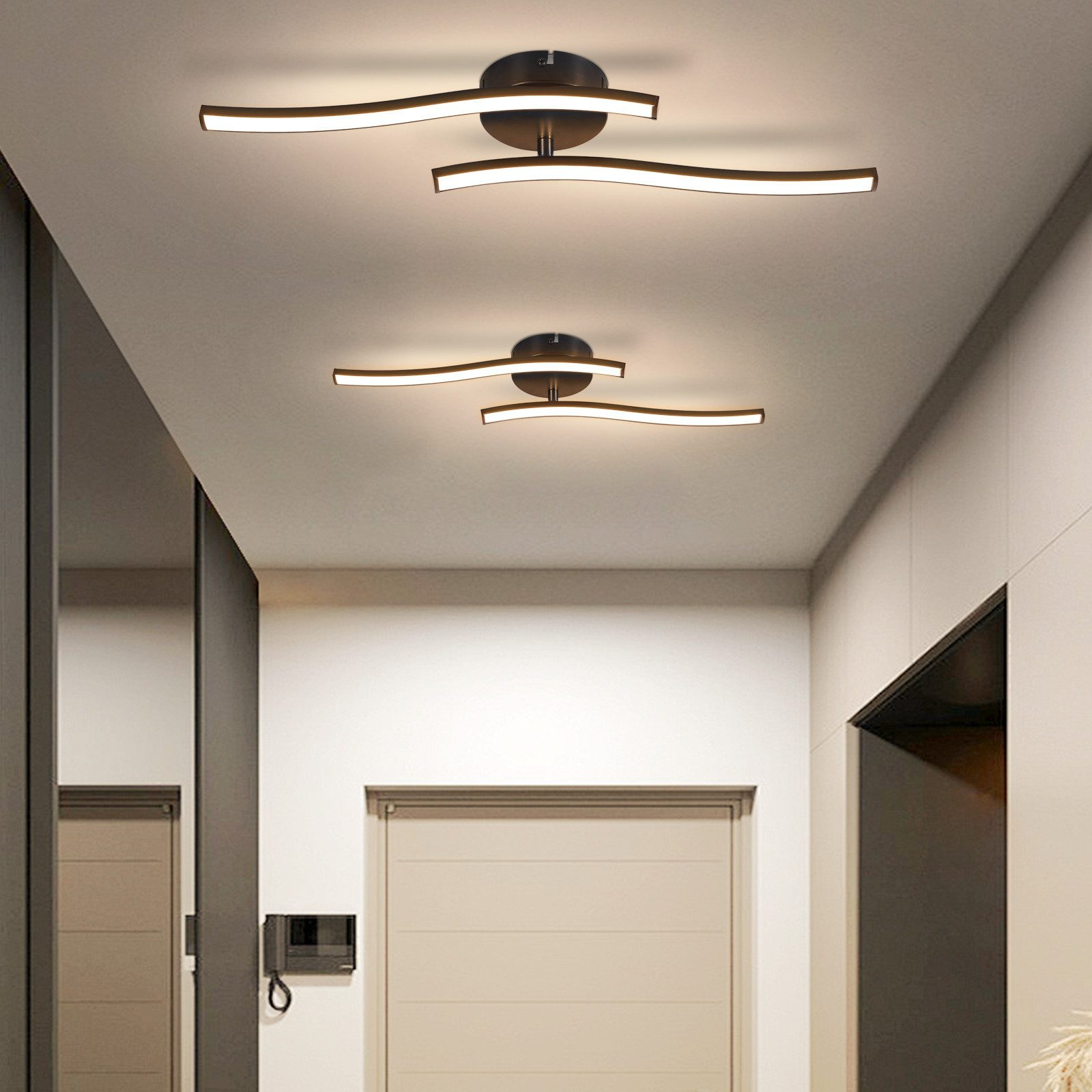 Due moderne plafoniere contro un soffitto bianco. Le luci hanno un design elegante a forma di onda.
