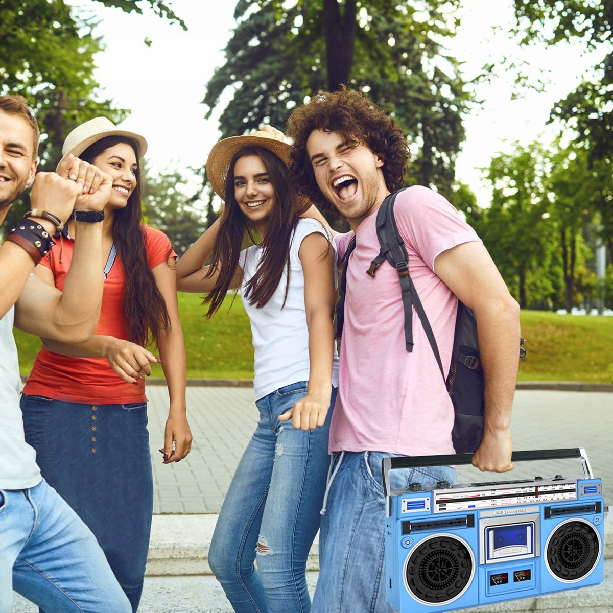 Eine Gruppe Freunde tanzen und lächeln, mit einer blauen Boombox. Bäume und grünes Gras im Hintergrund.