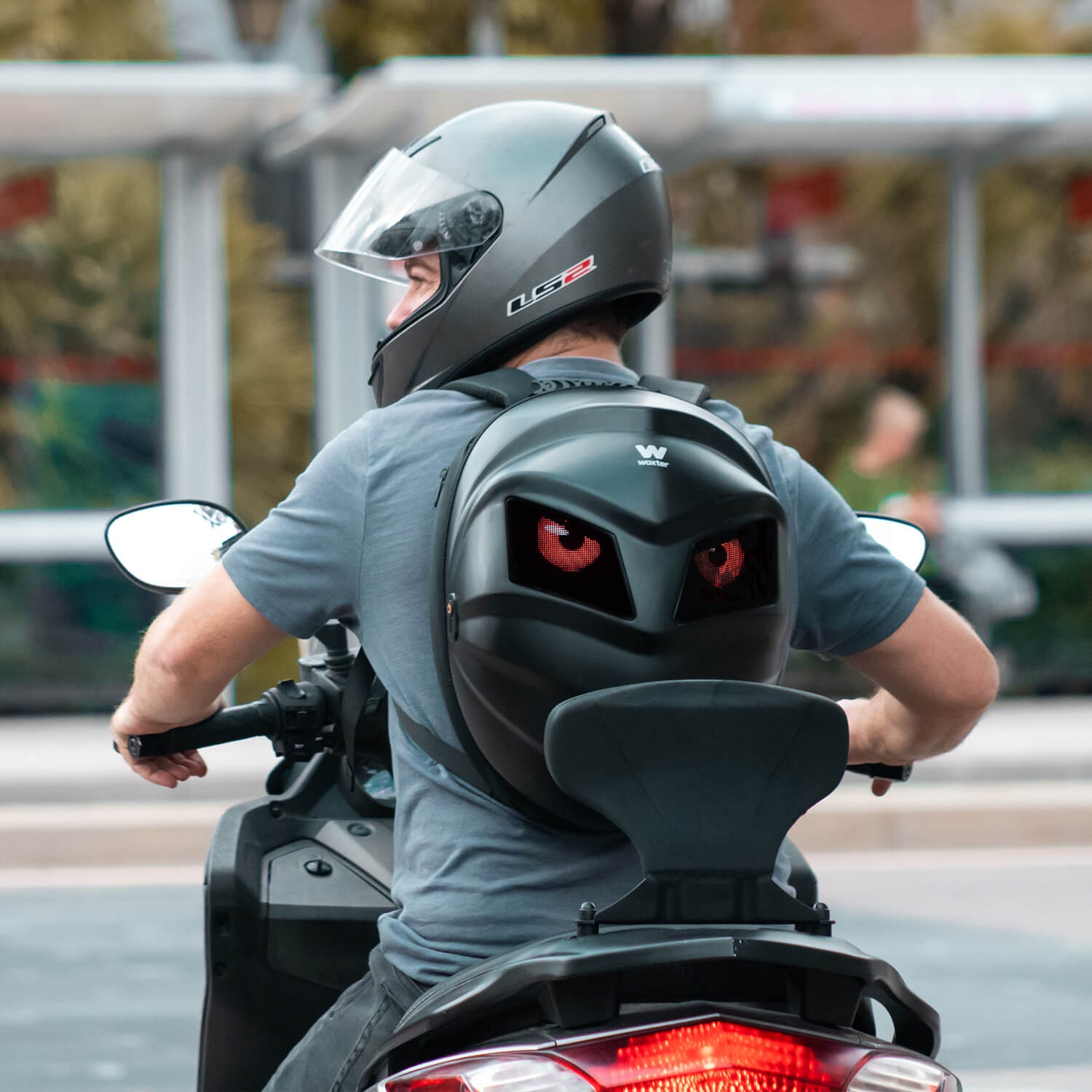 Una persona en un scooter que usa un casco con ojos rojos en una mochila.