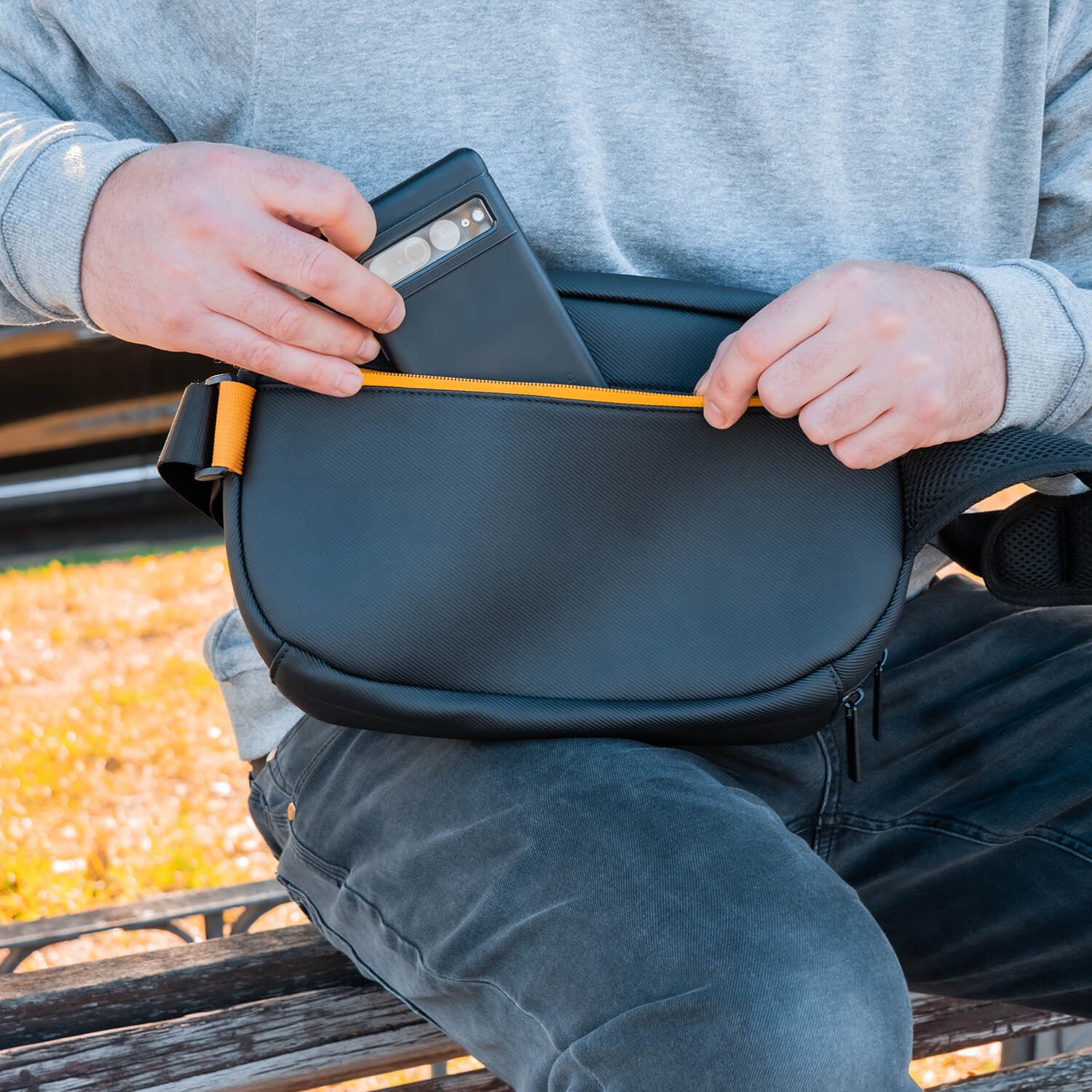 Persona guardando un teléfono en una riñonera negra con detalles naranja.