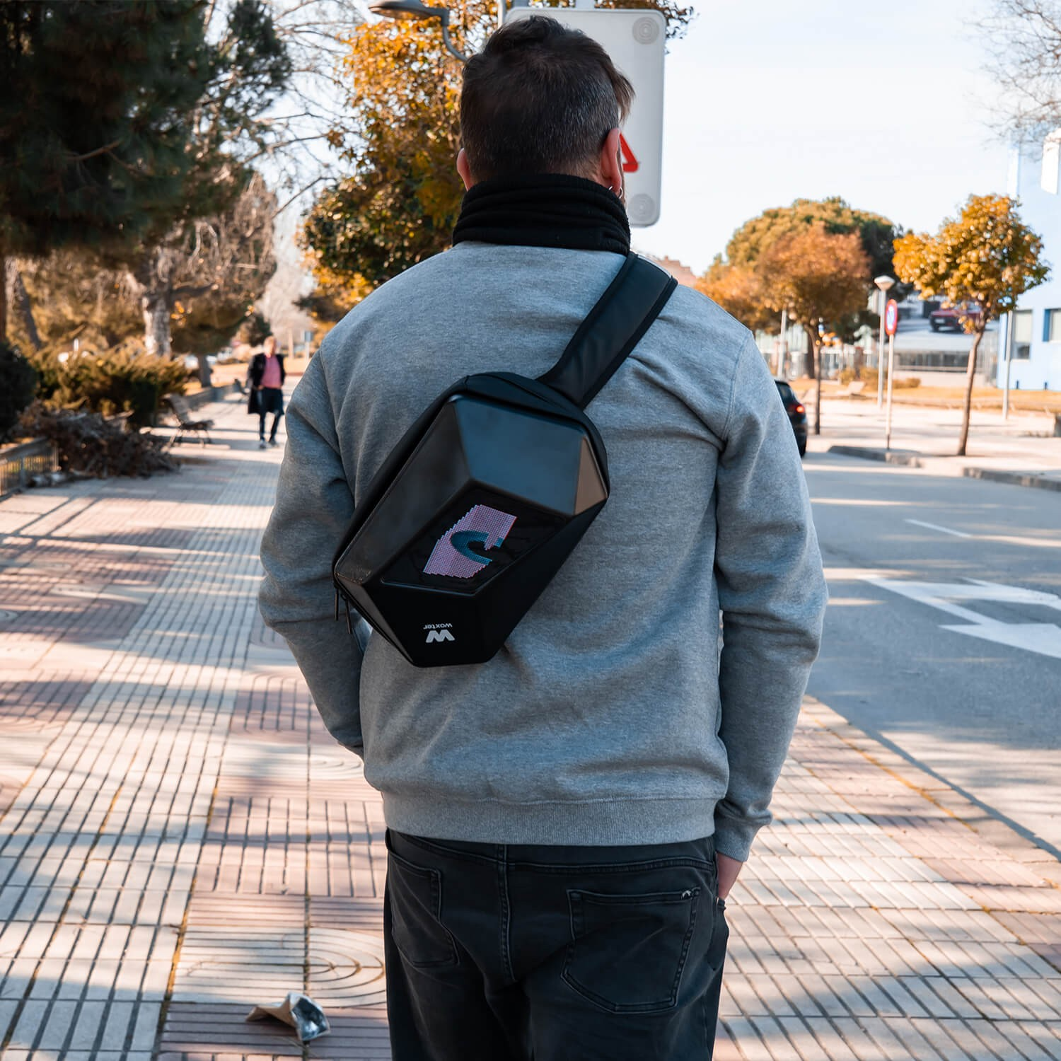 Una persona con un suéter gris y una bolsa negra en una acera.