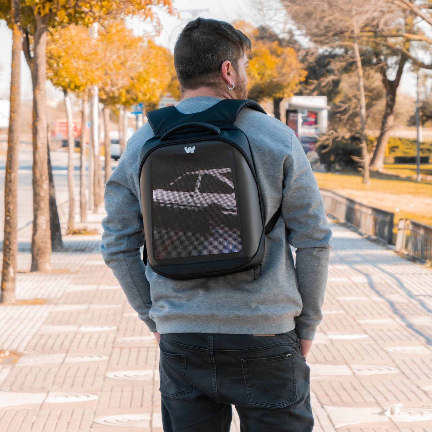 Un hombre que lleva una mochila negra con una pantalla que muestra un coche.