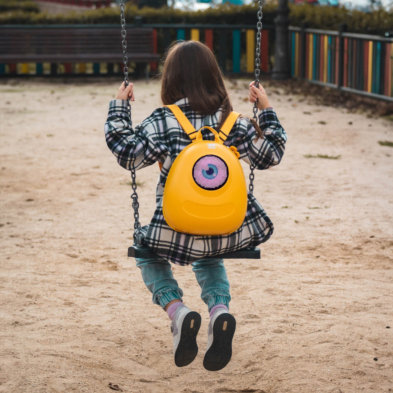 Niña en columpio con mochila amarilla. Fondo de parque infantil.