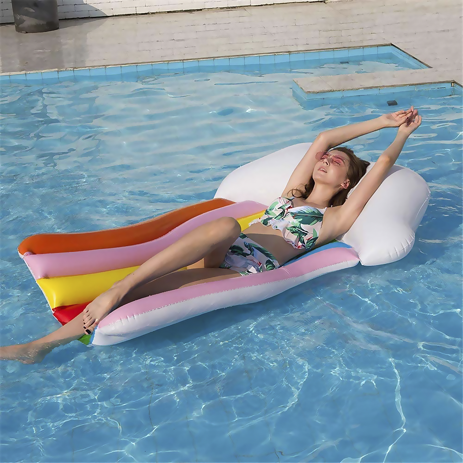 Mujer en piscina, sobre inflable, brazos arriba, gafas de sol.