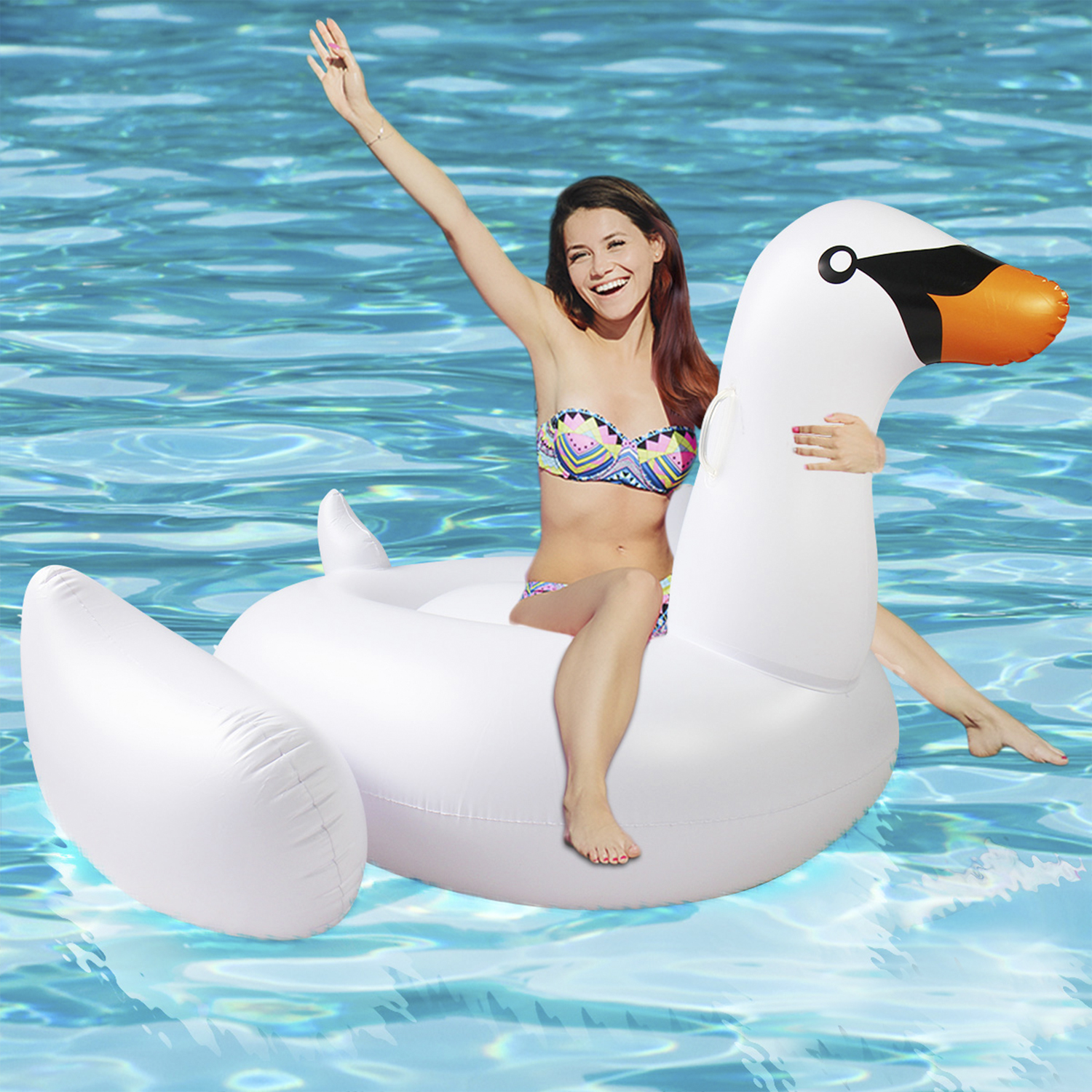 Una mujer en bikini sentada en un flotador de cisne blanco en una piscina.