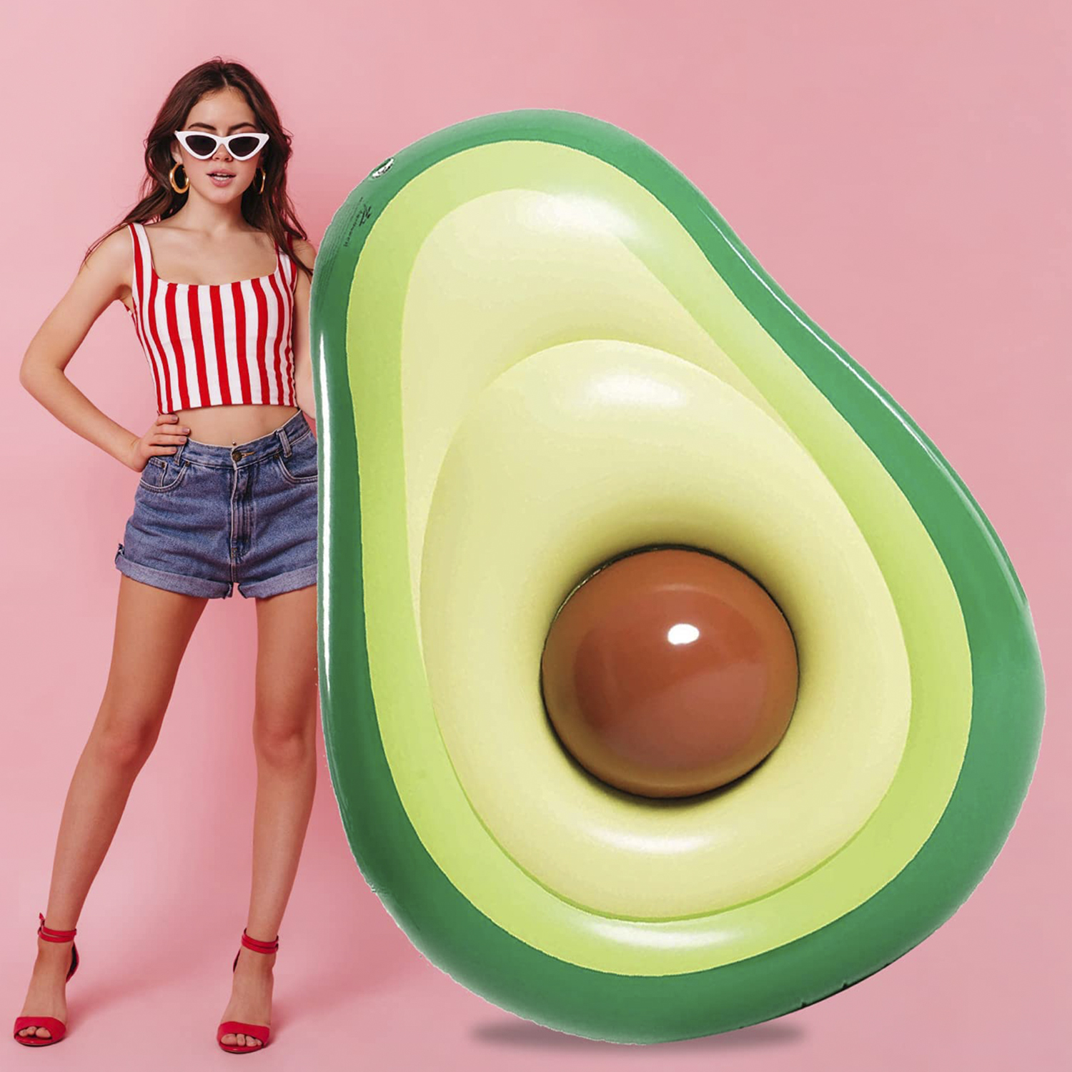 Mujer con top a rayas rojo y blanco junto a un flotador de aguacate. Fondo rosa.