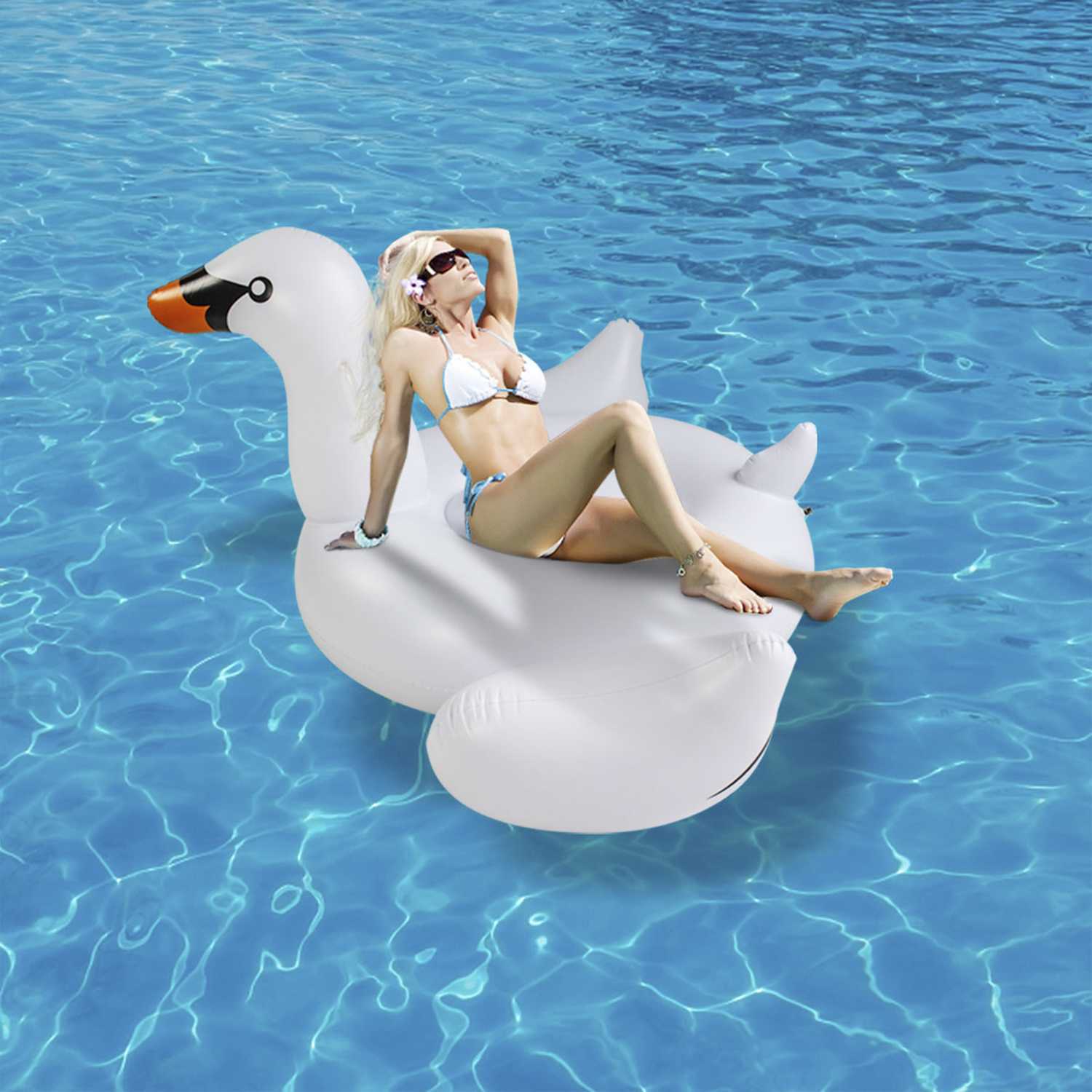 Mujer en un flotador de cisne blanco en agua azul. Lleva bikini y gafas de sol, tomando el sol en el flotador.