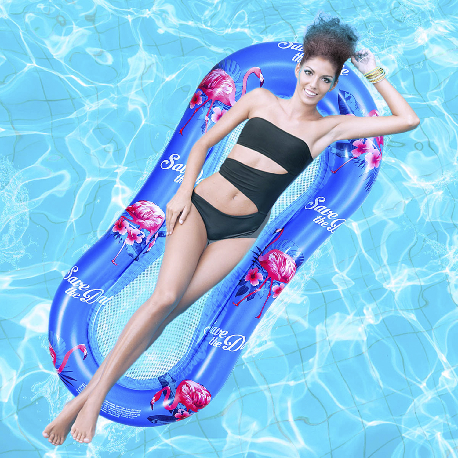 Mujer en flotador inflable azul con flamencos. Viste traje de baño negro y sonríe.