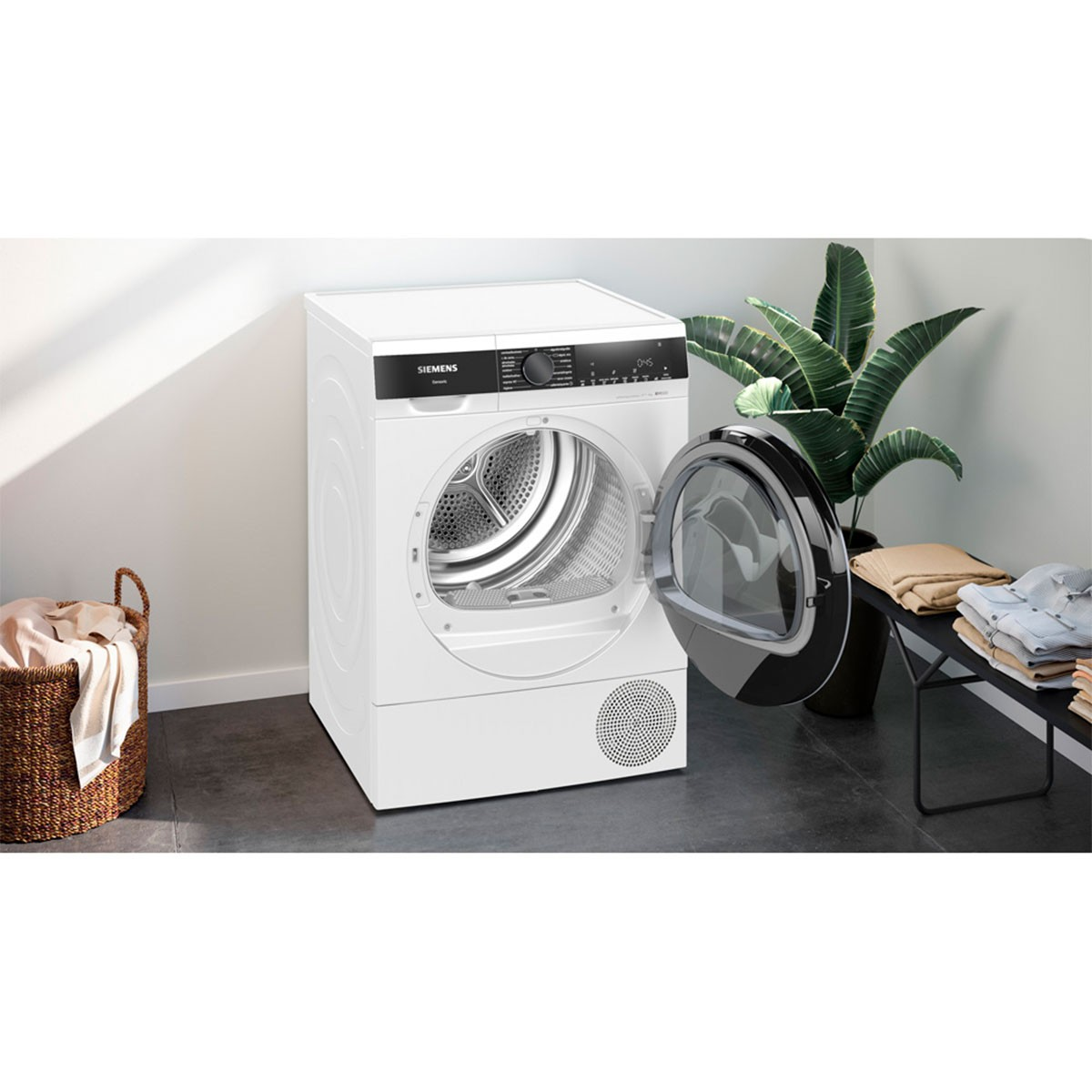 Secadora Siemens blanca con la puerta abierta. Una cesta de ropa y una planta están al lado.