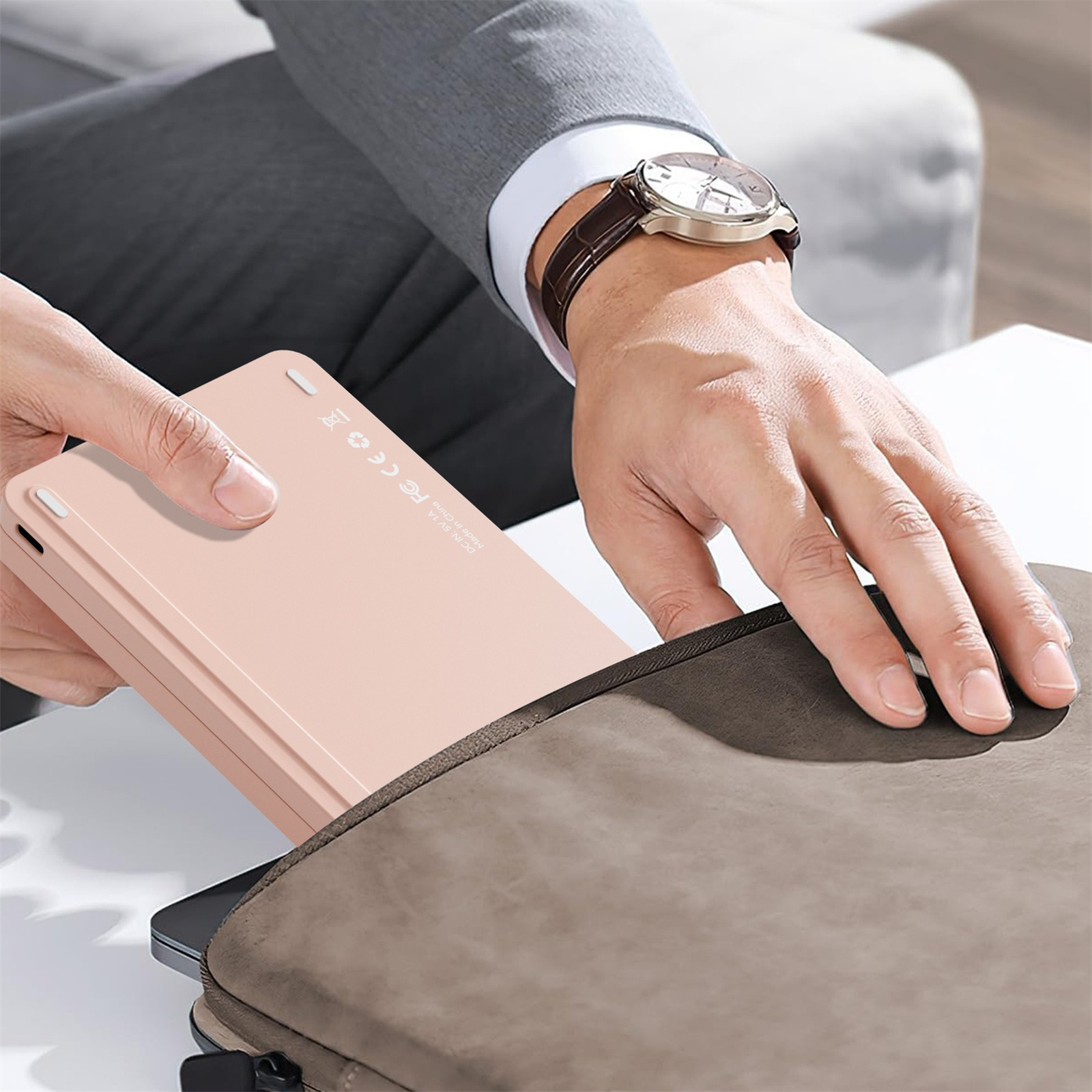 Die Hand einer Person, die ein rosa Tablet aus einer grauen Tragetasche nimmt, mit einer Uhr sichtbar.