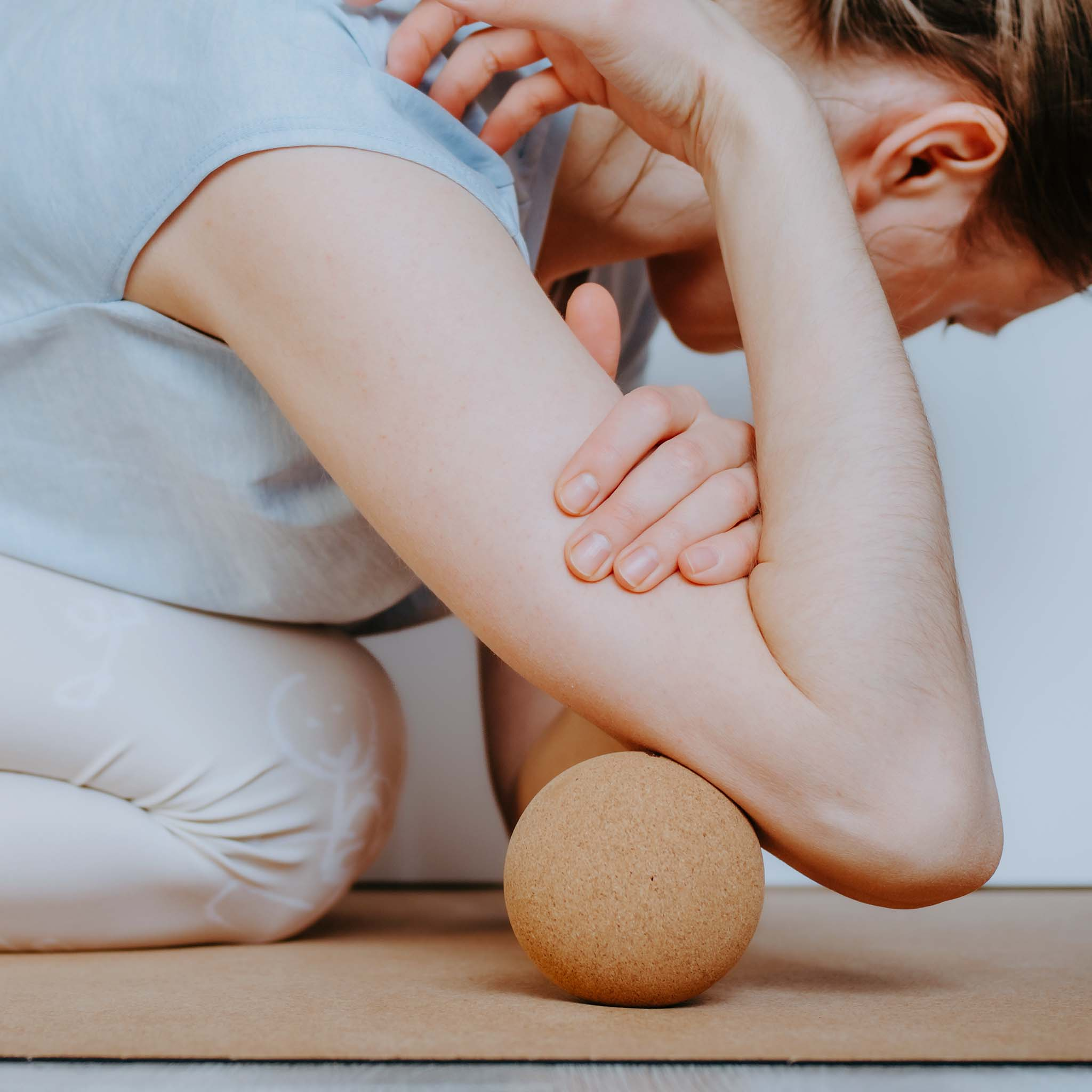 Eine Person massiert den Arm mit einem Ball. Die Person trägt ein blaues Hemd.