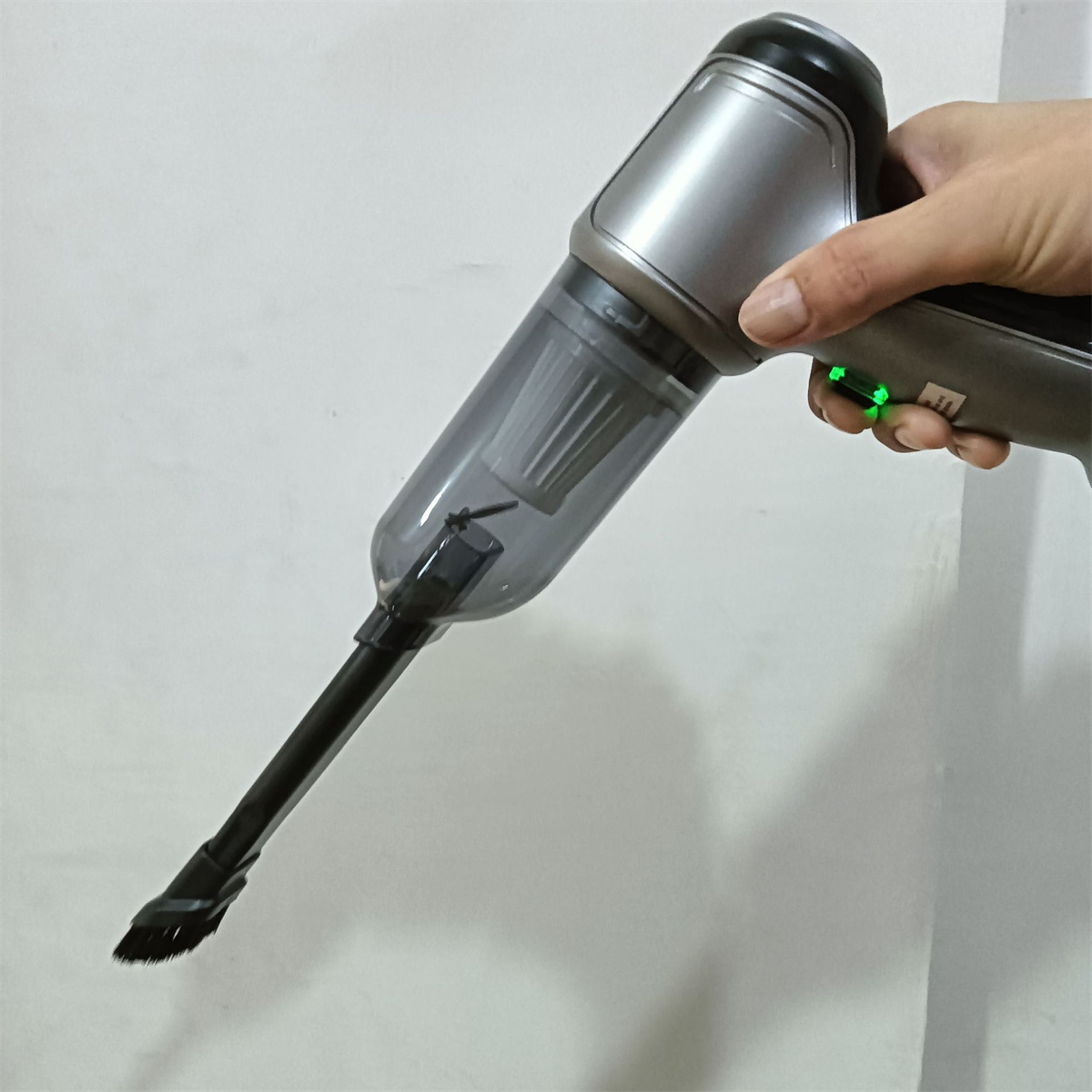 Hand hält einen silber-schwarzen Handstaubsauger, angewinkelt und einsatzbereit.