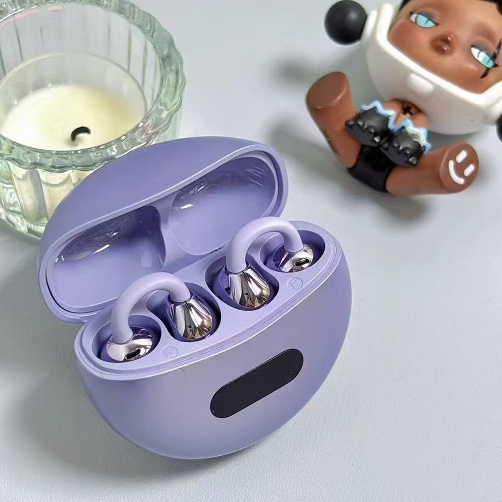 Ein lila Etui geöffnet mit drahtlosen Ohrhörern und einer kleinen Figur im Hintergrund.