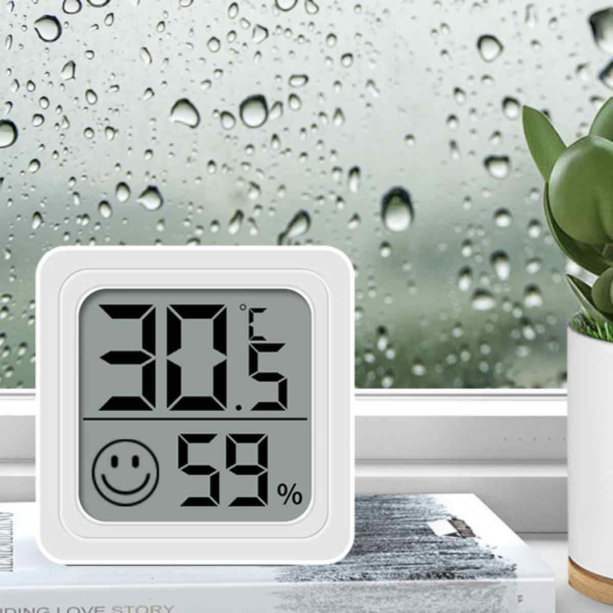 Ein digitales Thermometer zeigt 30,5 Grad und 59% an. Dahinter ein Fenster mit Regentropfen und Pflanze.