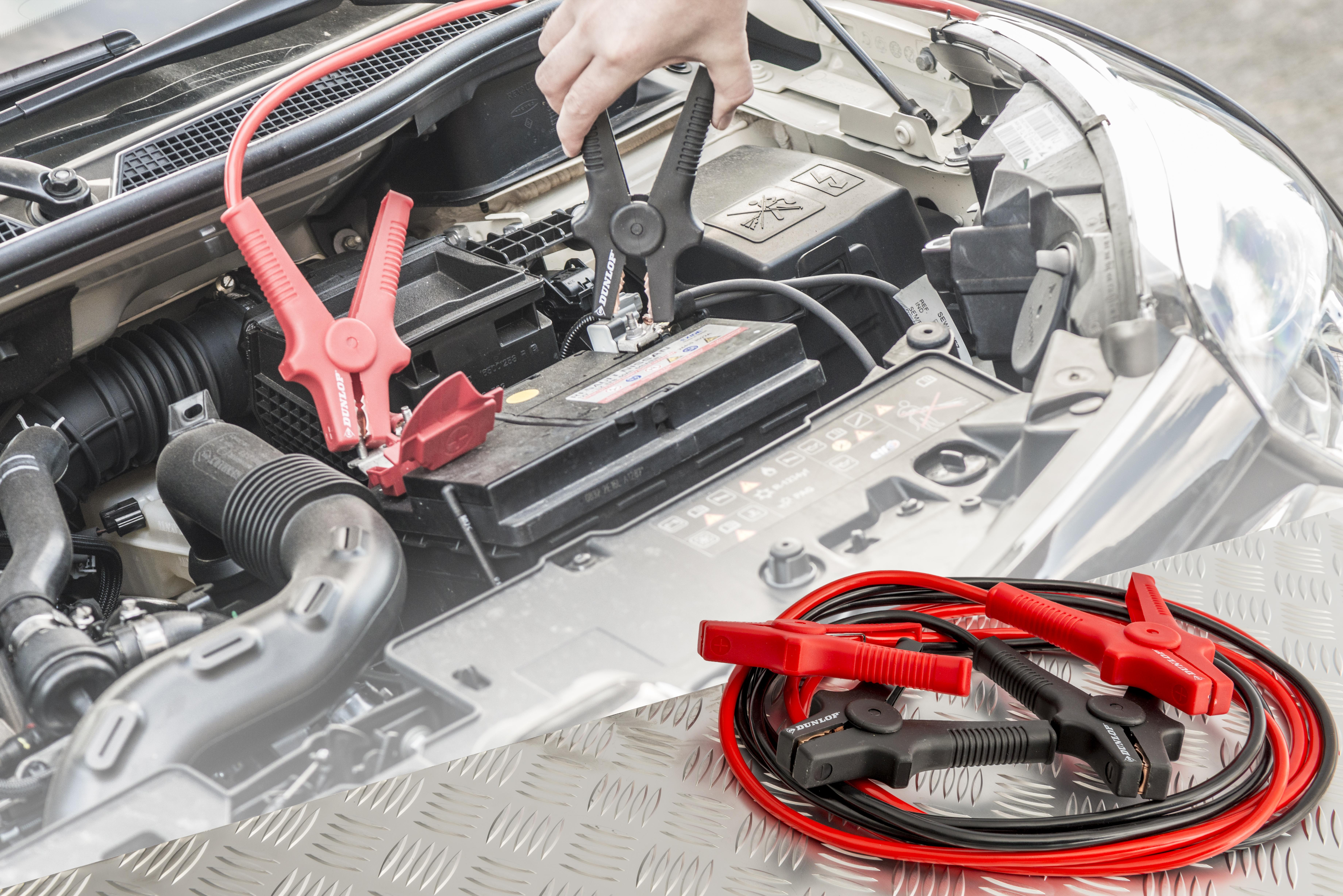 Car battery being jump-started with jumper cables. Hands connecting clamps.