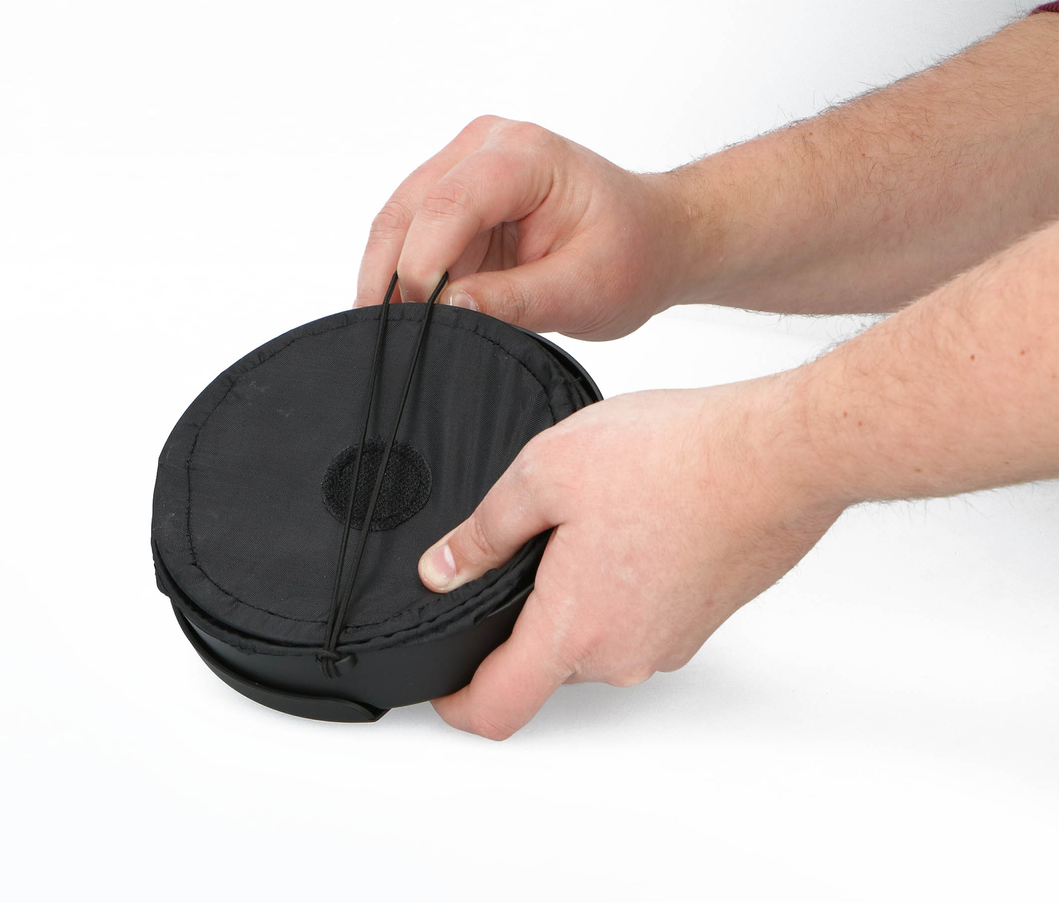 Handen die een zwarte, ronde opbergcase met ritssluiting vasthouden. Op een witte achtergrond.