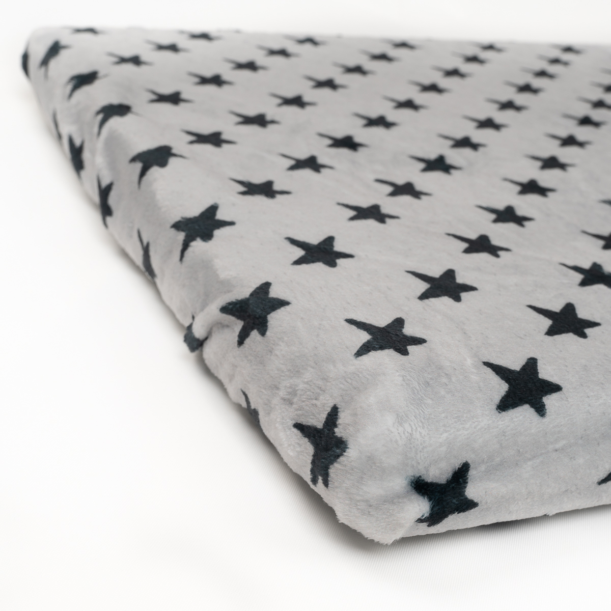 Manta de felpa gris con patrón de estrellas azul oscuro. Está sobre un fondo blanco.
