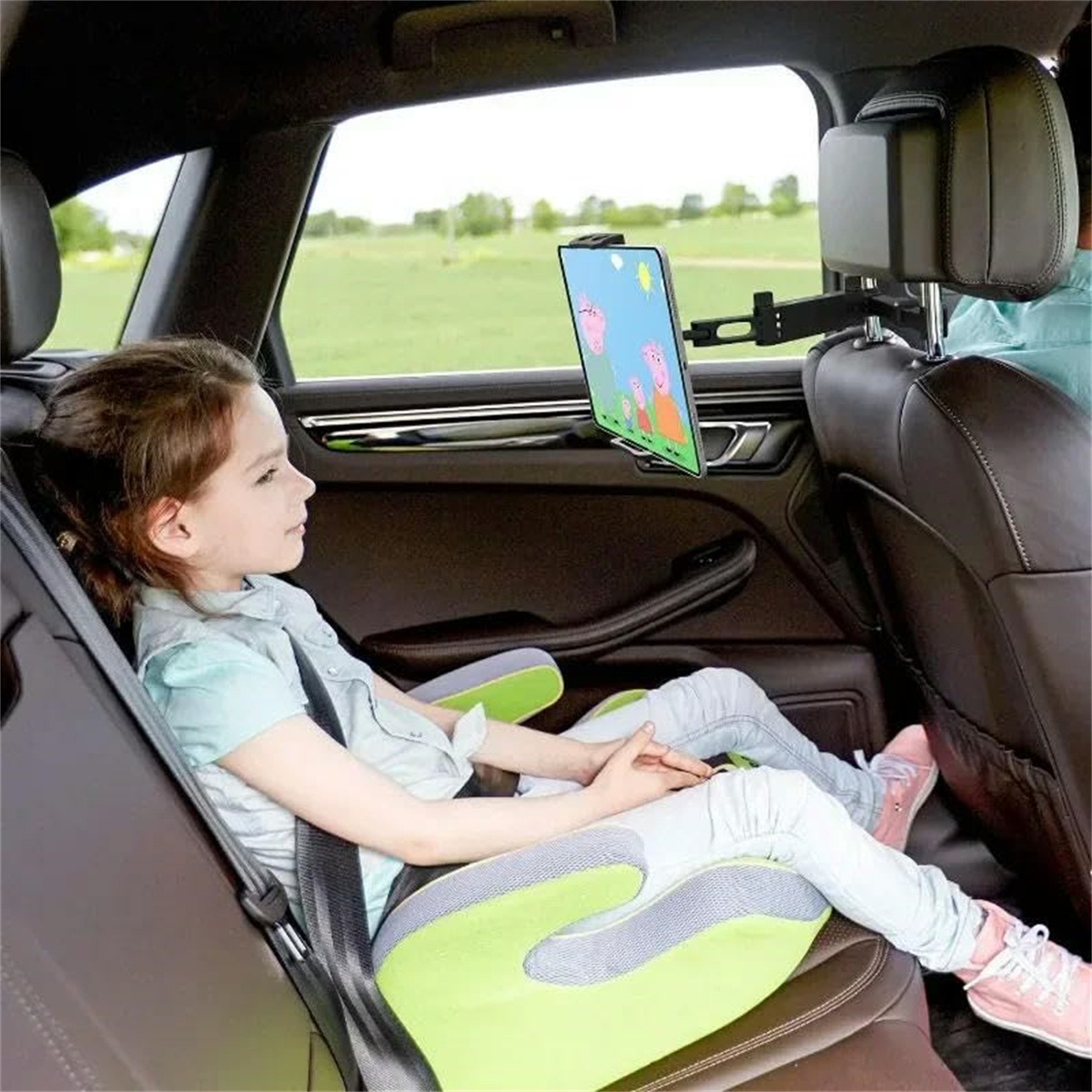 Ein junges Mädchen schaut auf ein Tablet, das an einer Kopfstütze im Auto befestigt ist. Sie sitzt in einem Kindersitz.