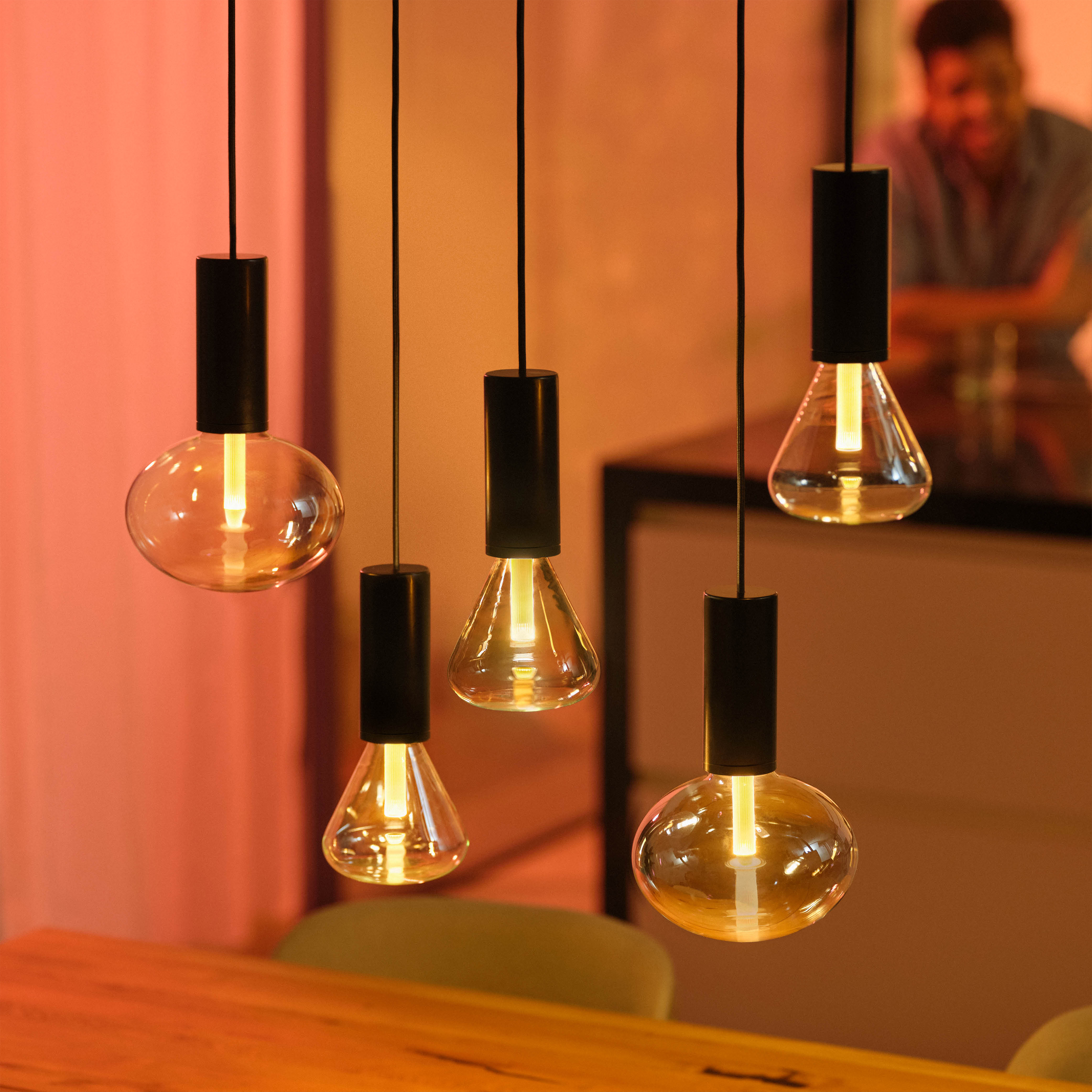 Cinco lámparas colgantes modernas con bombillas Edison. Accesorios negros, luz cálida, interiorismo.