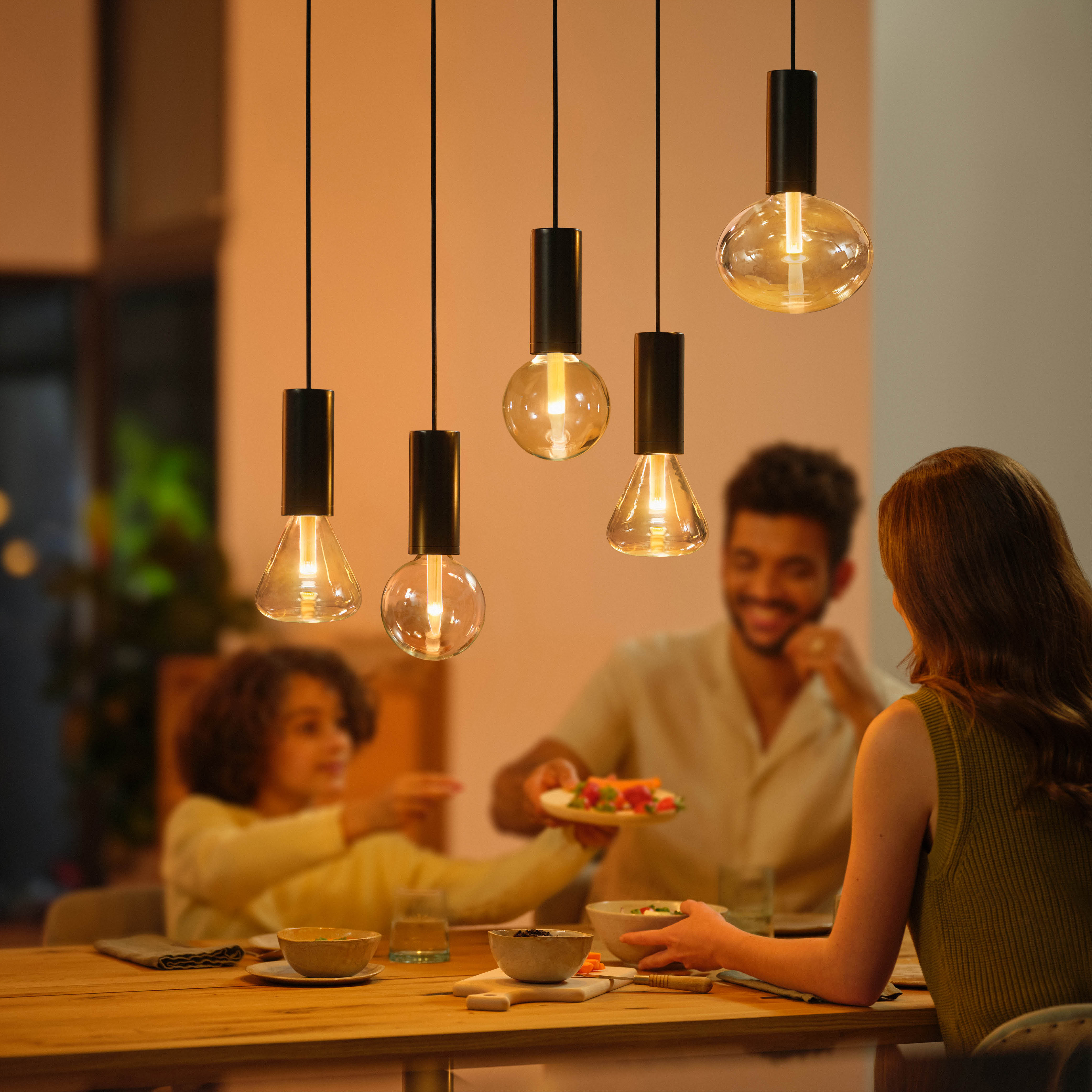 Comida familiar. Cinco lámparas colgantes sobre una mesa. Familia comiendo junta.