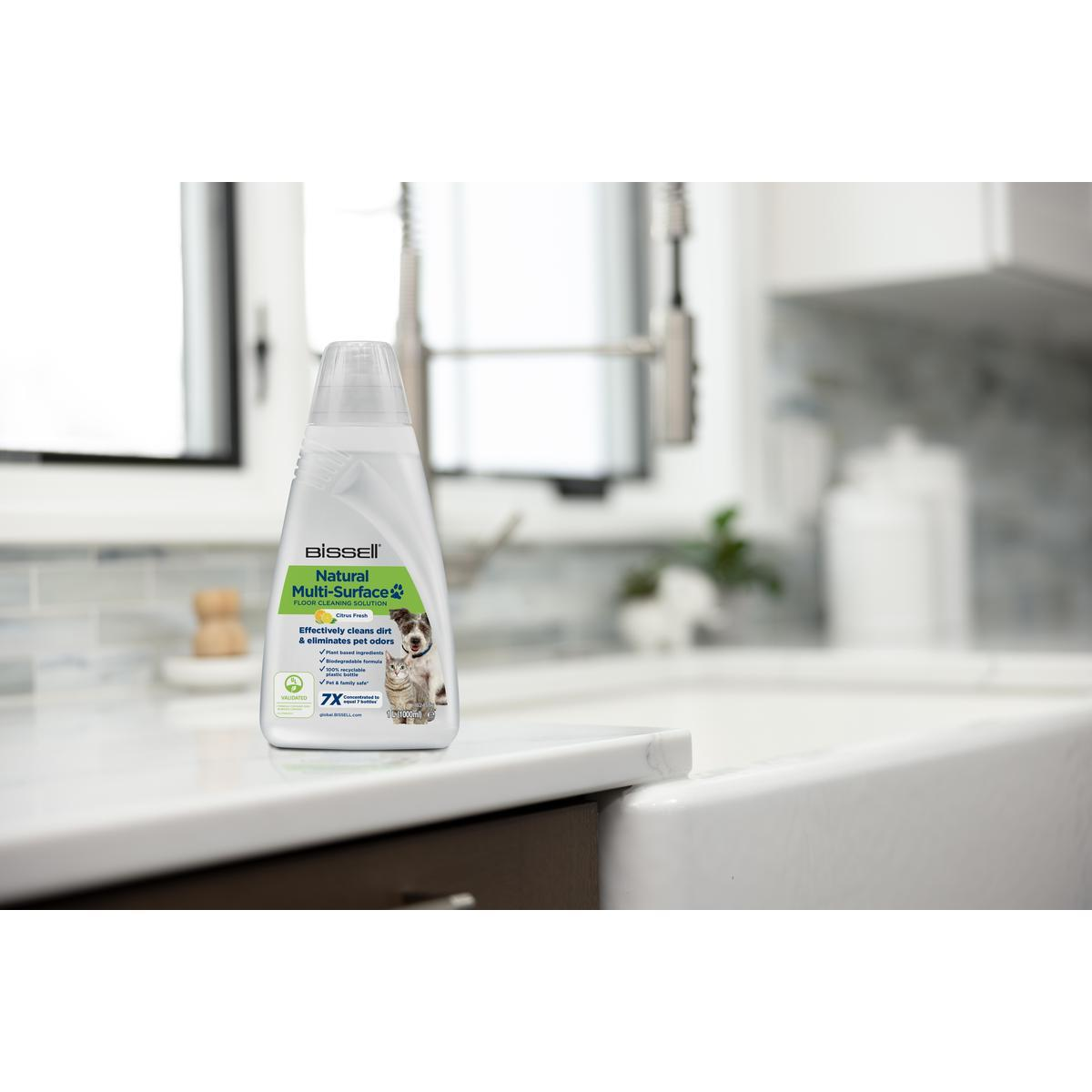Une bouteille de nettoyant Bissell Natural Multi-surface, avec un évier de cuisine et une fenêtre en arrière-plan.