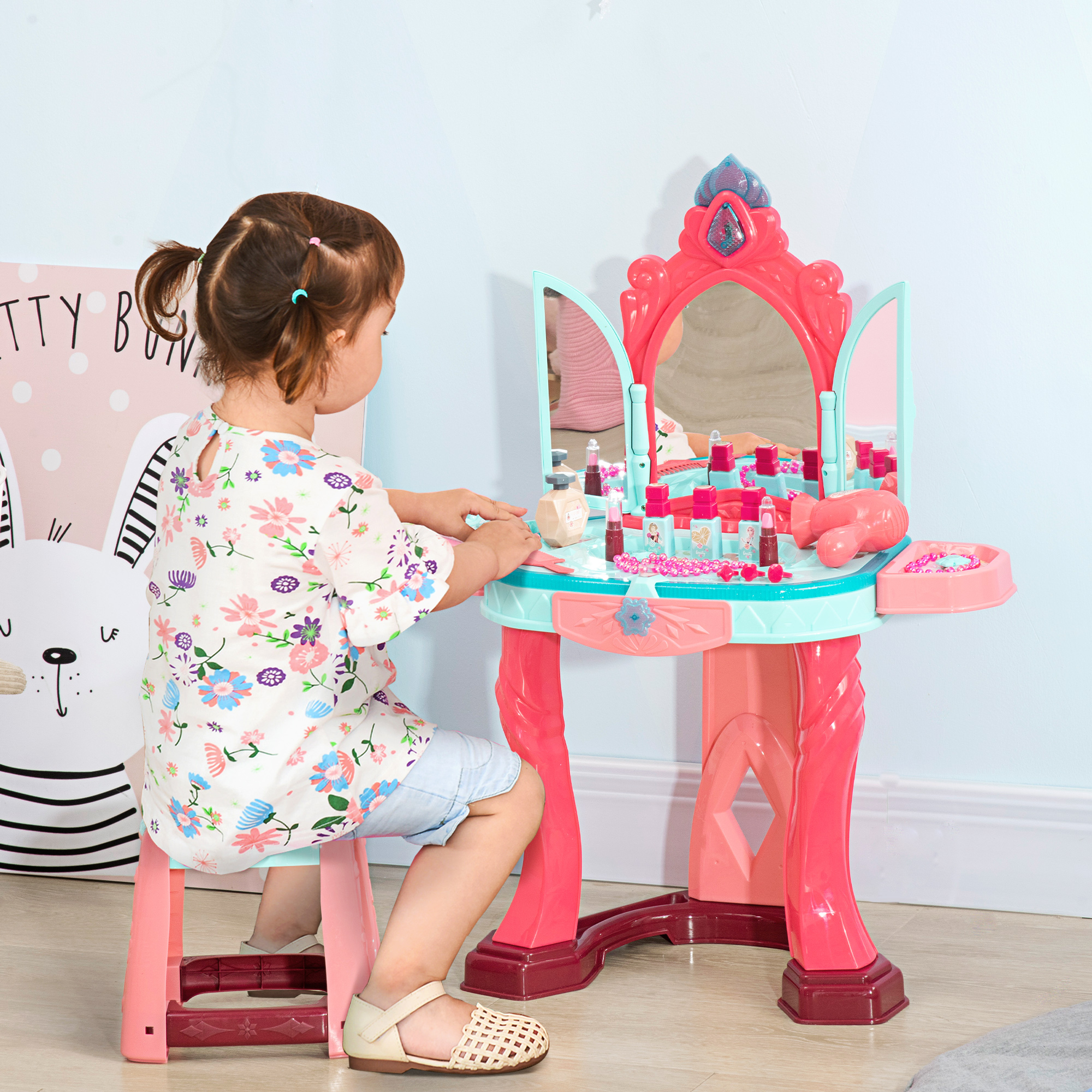 Una bambina che gioca con una toeletta giocattolo. Ha uno specchio, trucco e uno sgabello. Colori rosa e blu.