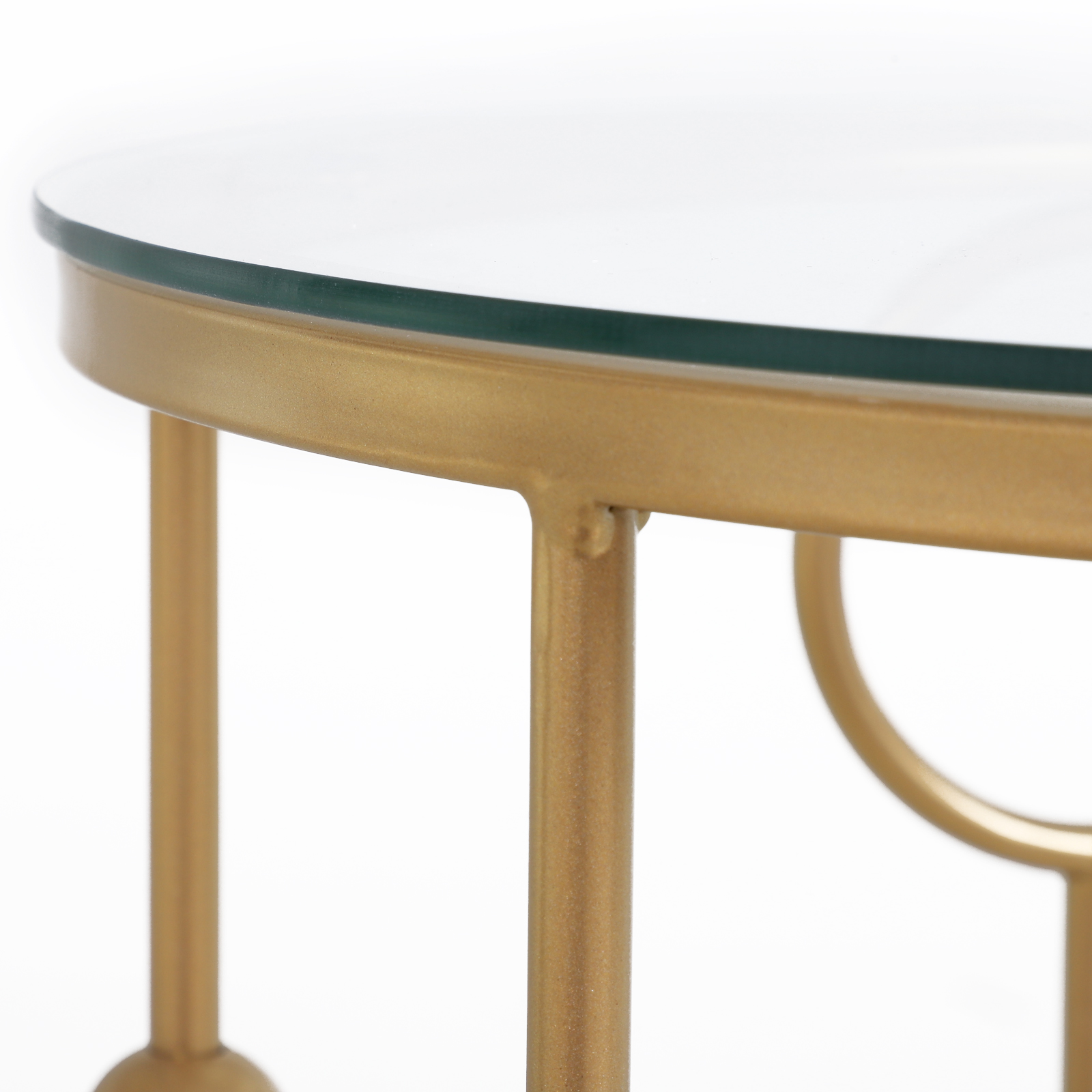 Un primo piano di un tavolo rotondo dorato con piano in vetro su sfondo bianco.