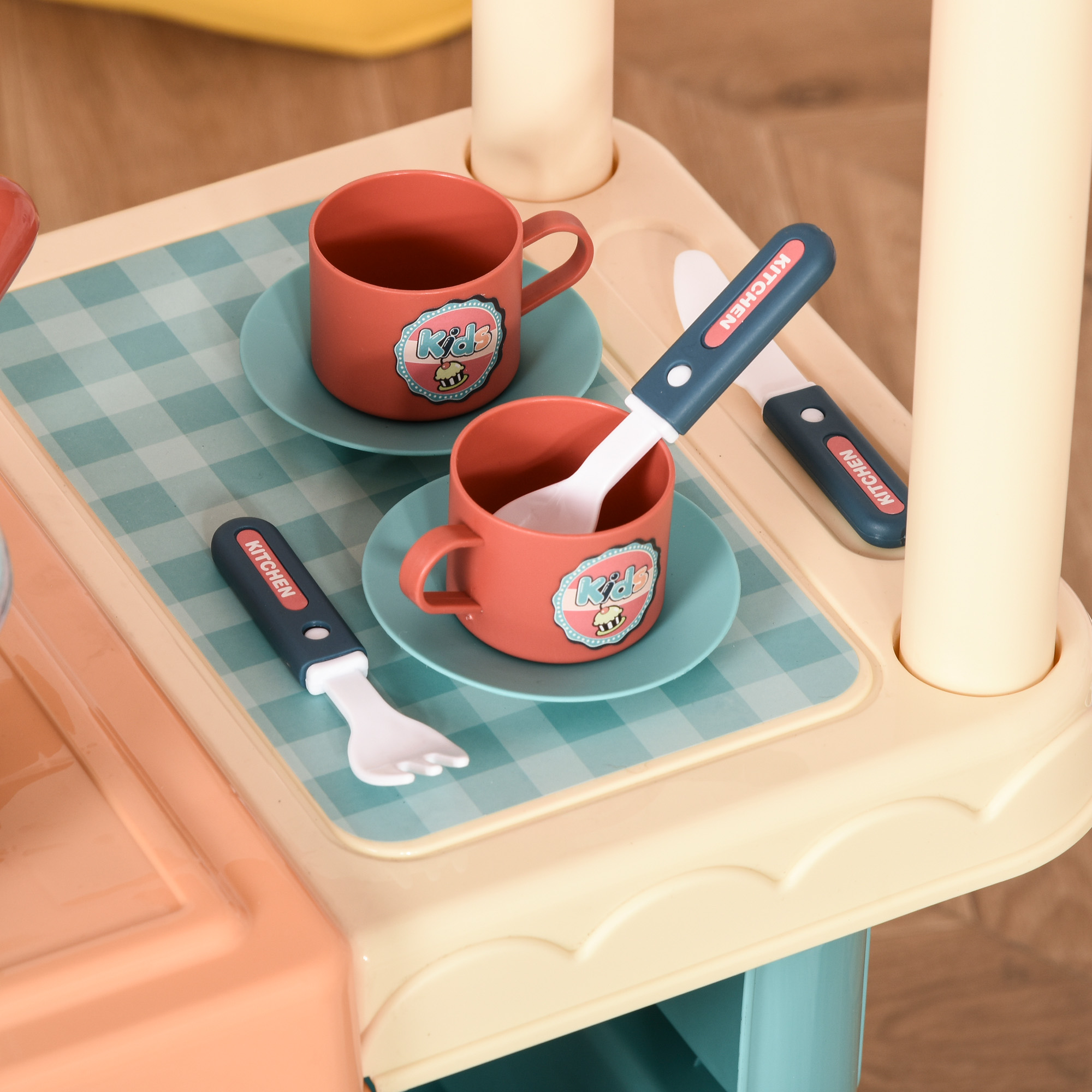 Un primo piano di un set da cucina giocattolo con due tazze rosse su piattini e utensili di plastica. Lo sfondo è sfocato.