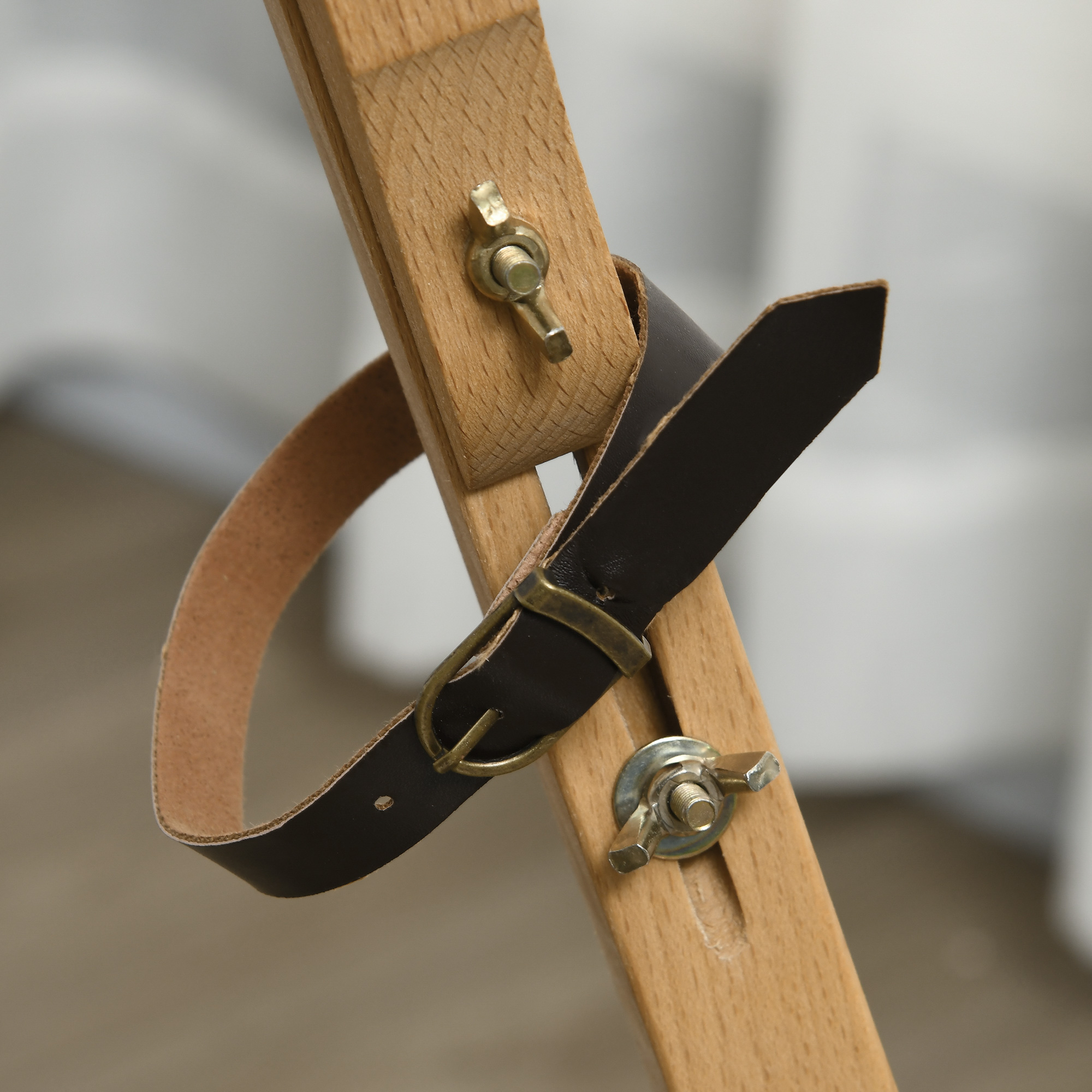 Primo piano di un cavalletto in legno con un cinturino in pelle e elementi di fissaggio in metallo.