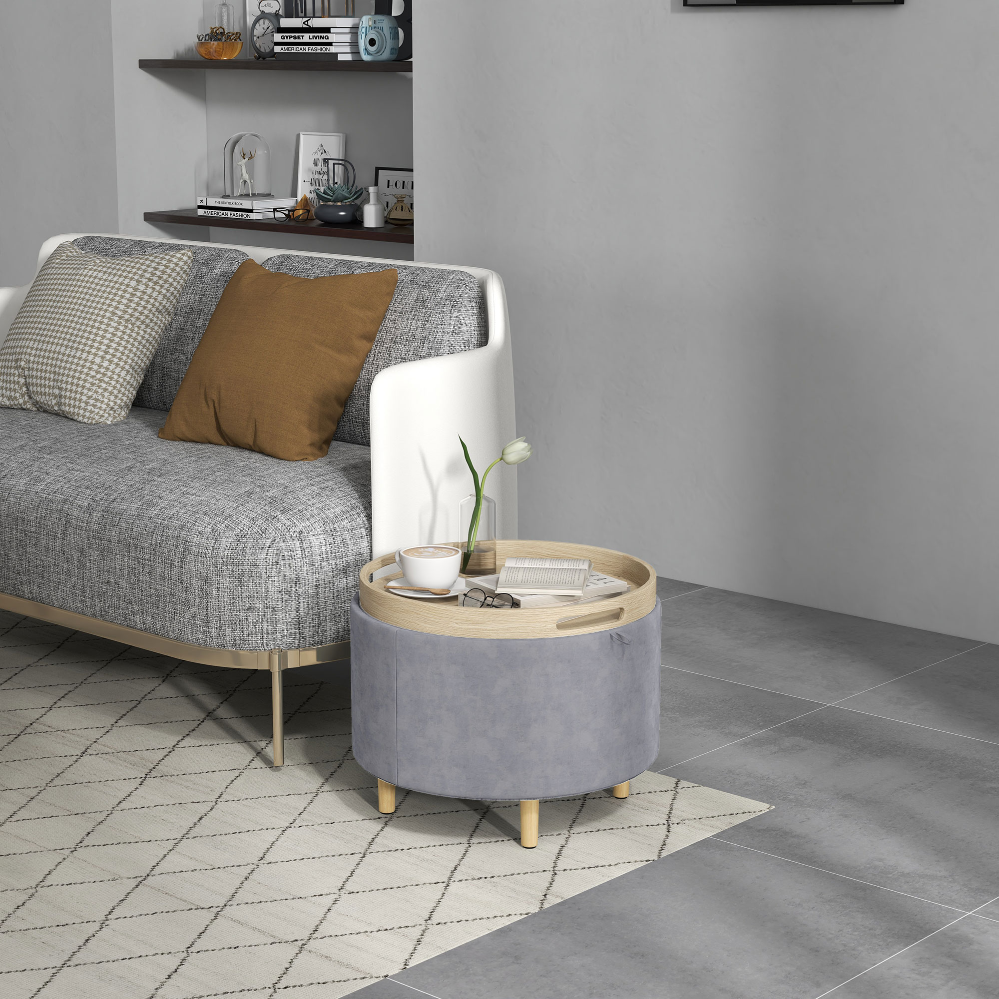 Un pouf rotondo grigio con un vassoio sopra. Un divano e mensole sullo sfondo.