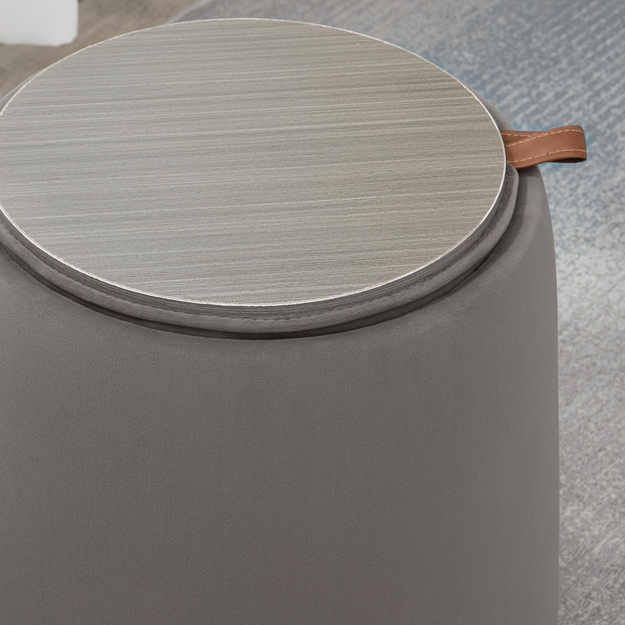 Pouf rotondo grigio con piano in legno. Maniglia in pelle sul lato.