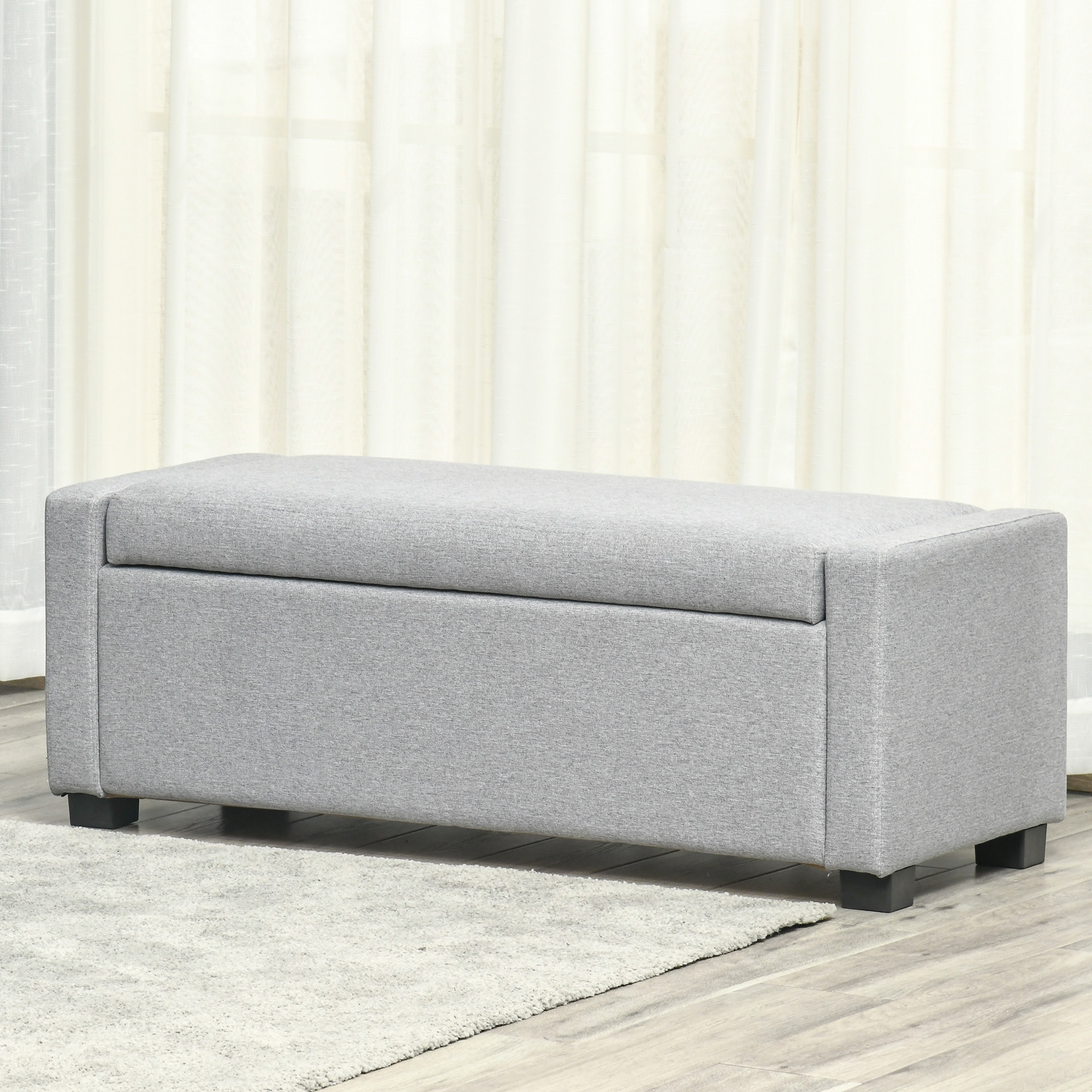 Panca contenitore grigia con coperchio, su un tappeto chiaro.