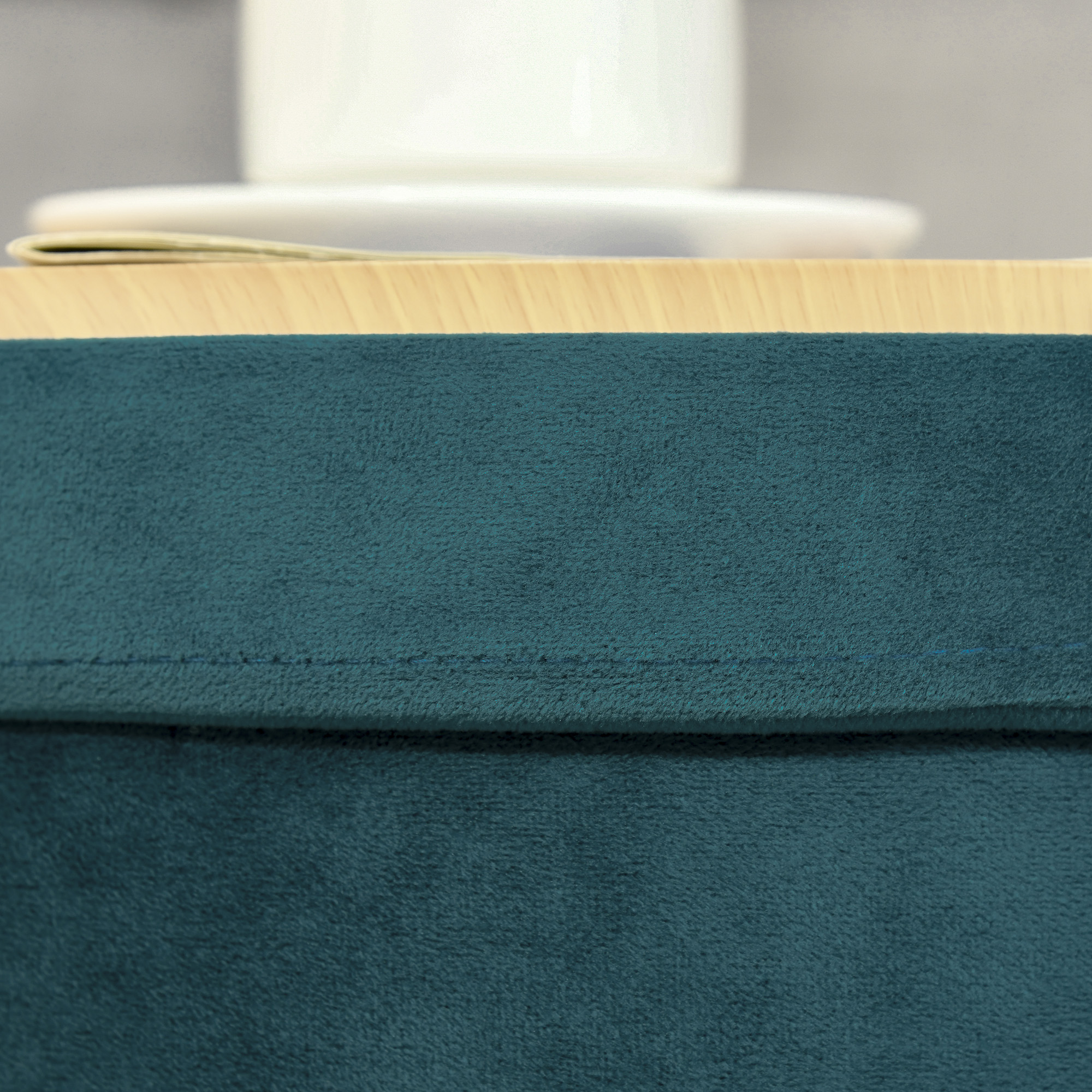 Primo piano di una coperta color teal su un tavolo di legno. Una tazza e un piattino bianchi sono sulla coperta.