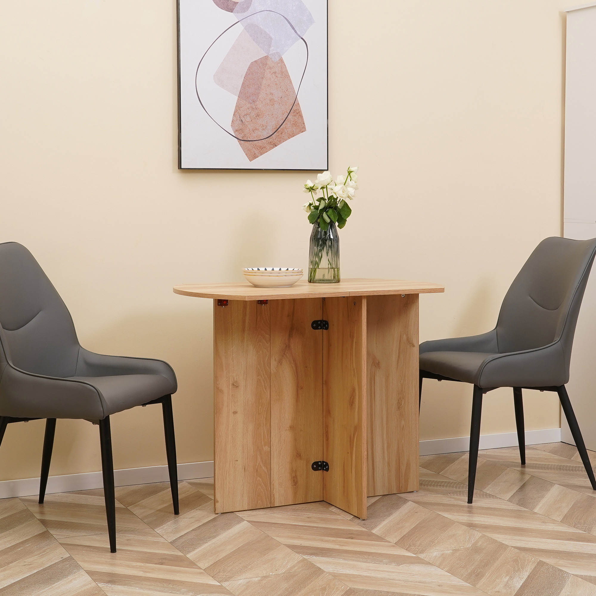 Un tavolo di legno con sedie, un vaso con fiori e un quadro appeso al muro. Le sedie sono grigie.
