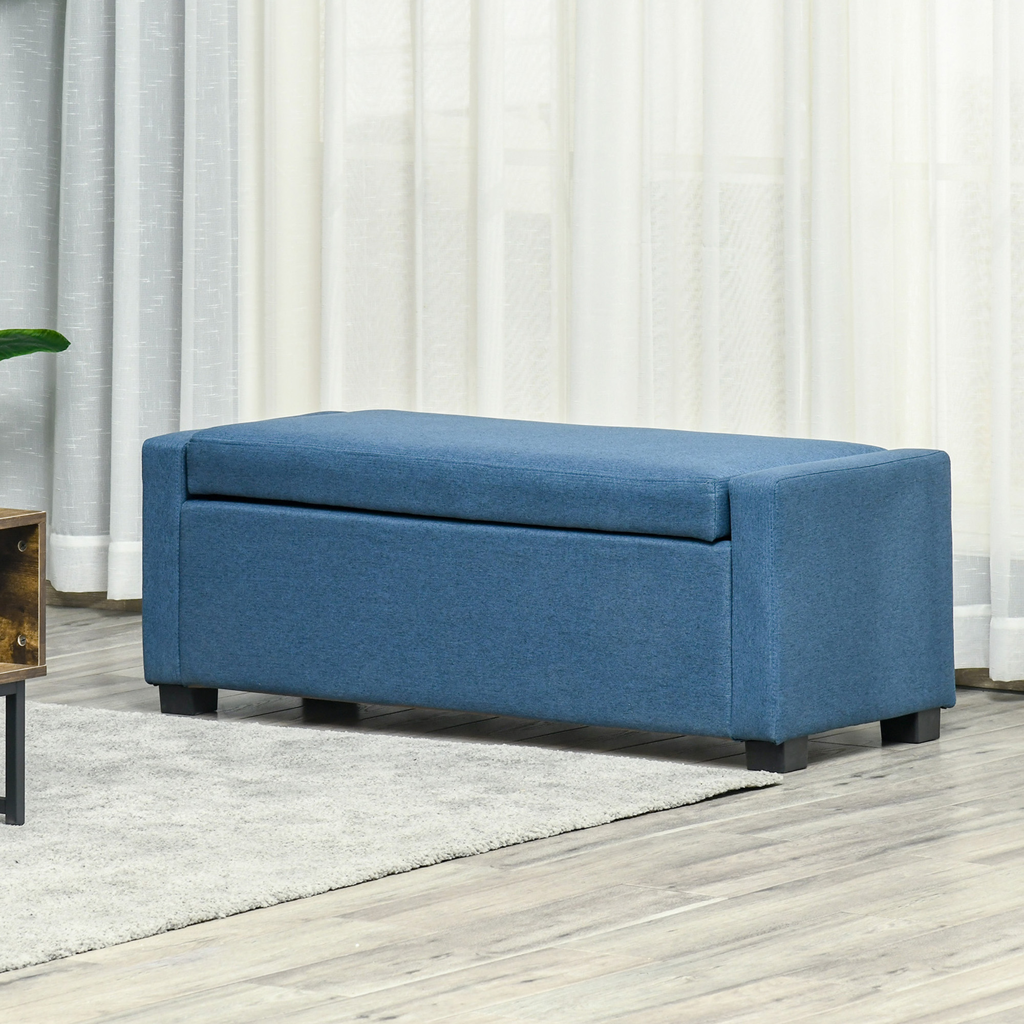 Un pouf contenitore blu con coperchio su un tappeto chiaro e pavimento in legno.
