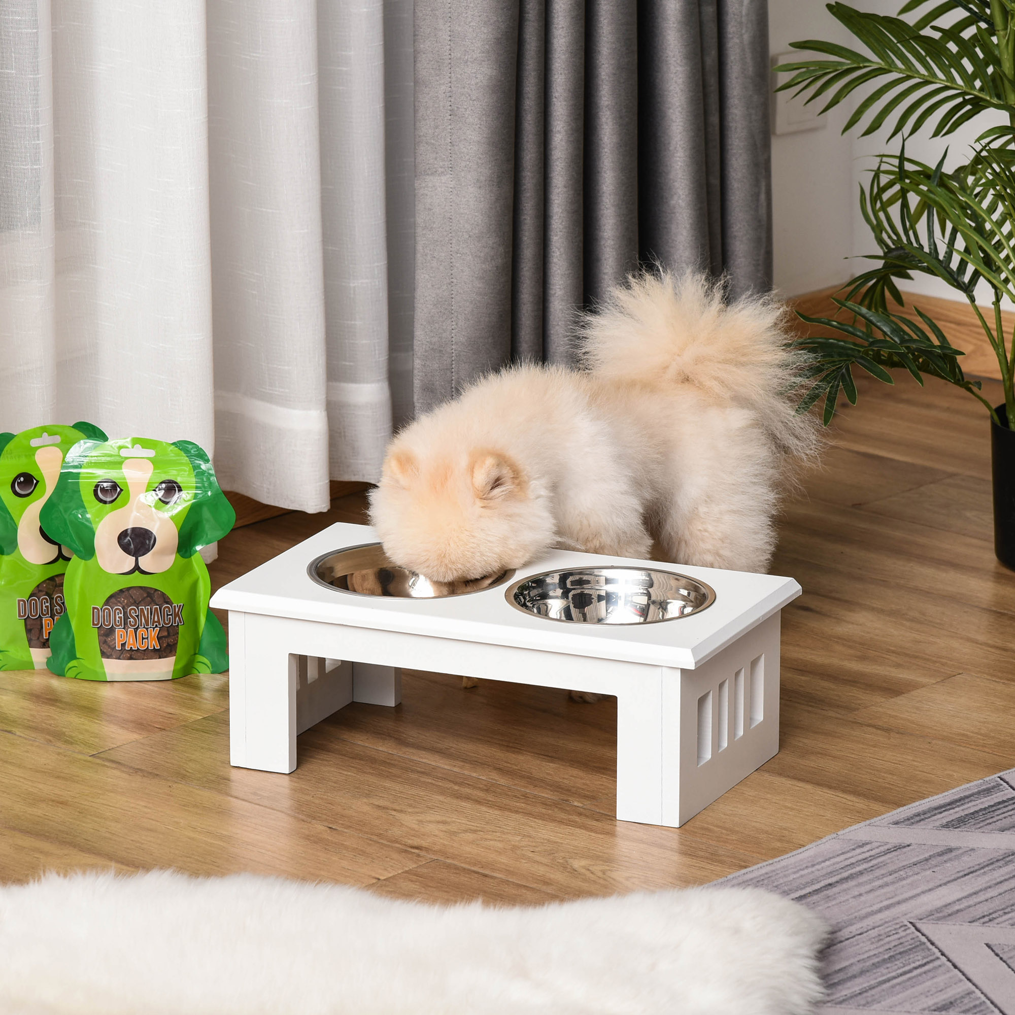 Kleiner Hund, der aus einem weißen Hundenapfständer frisst. Grüne Hundefutterbeutel daneben.