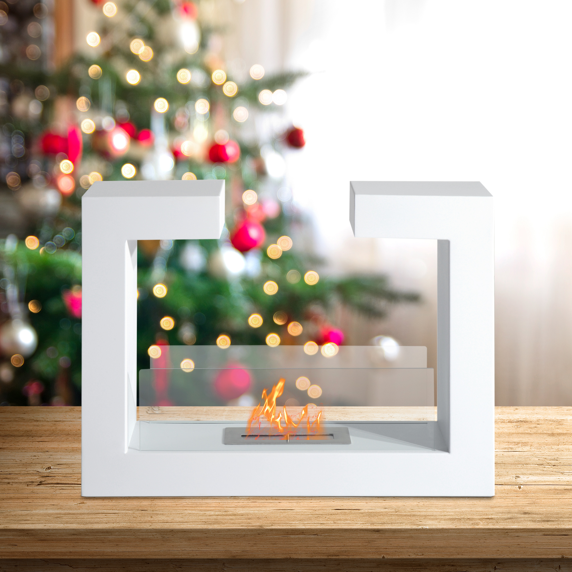 Caminetto bianco con fiamme, su un tavolo di legno, con un albero di Natale sfocato sullo sfondo.