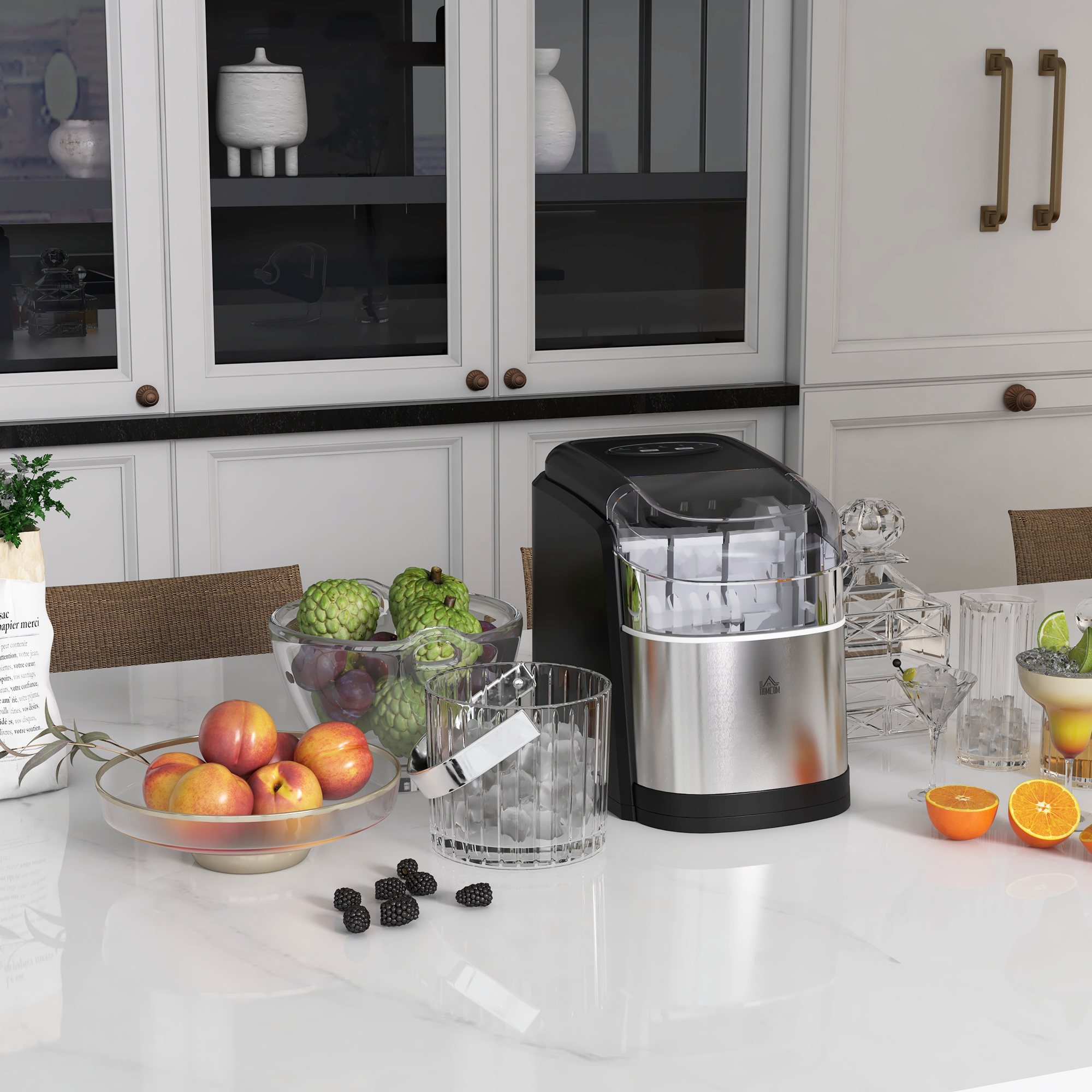 Scena cucina: macchina per il ghiaccio, ciotole di frutta, bicchieri e un mobile con ante bianche.