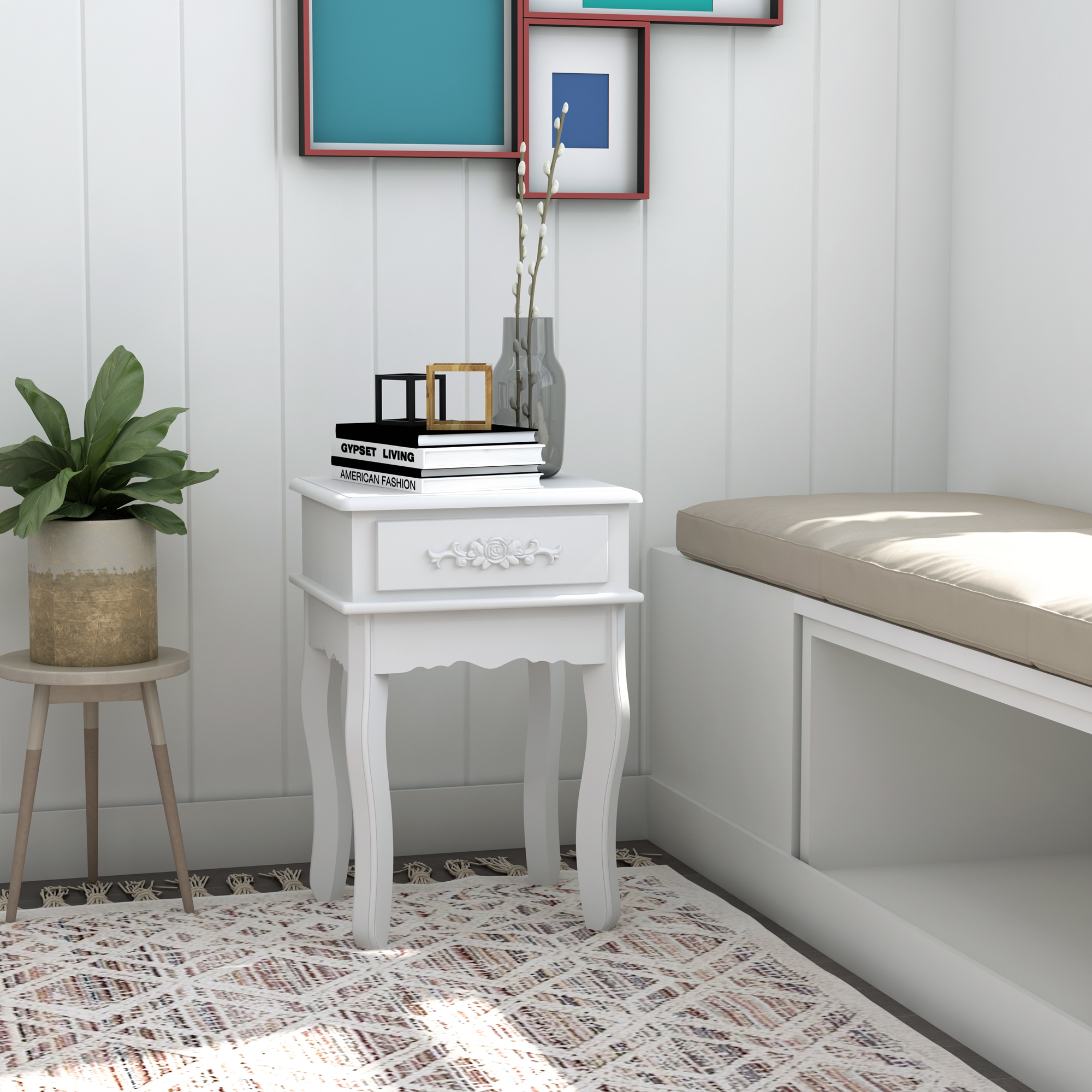 Mesita de noche blanca con cajón, libros y un jarrón de flores, contra una pared blanca.