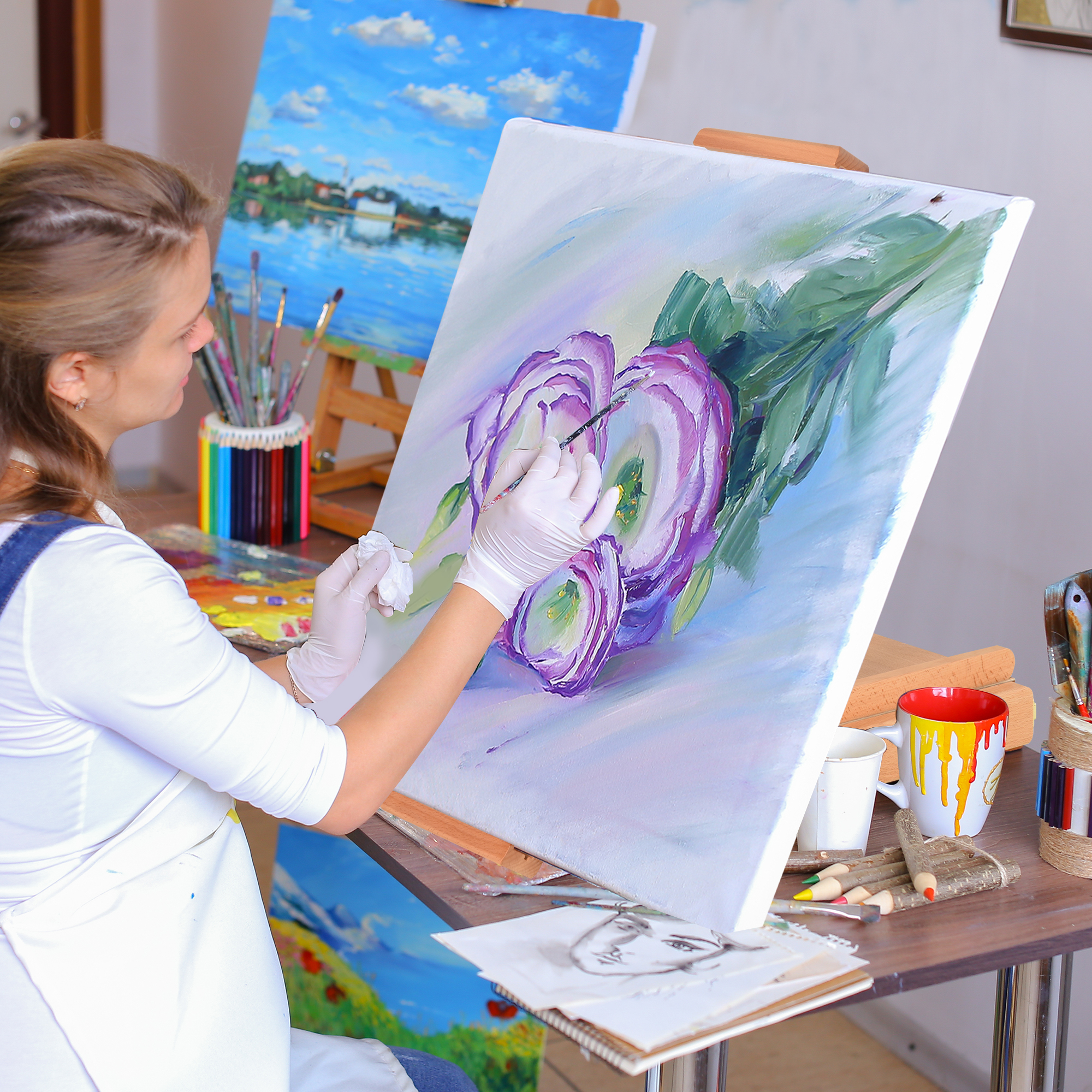 Donna che dipinge una grande tela con un disegno floreale. Colori e pennelli sul tavolo.