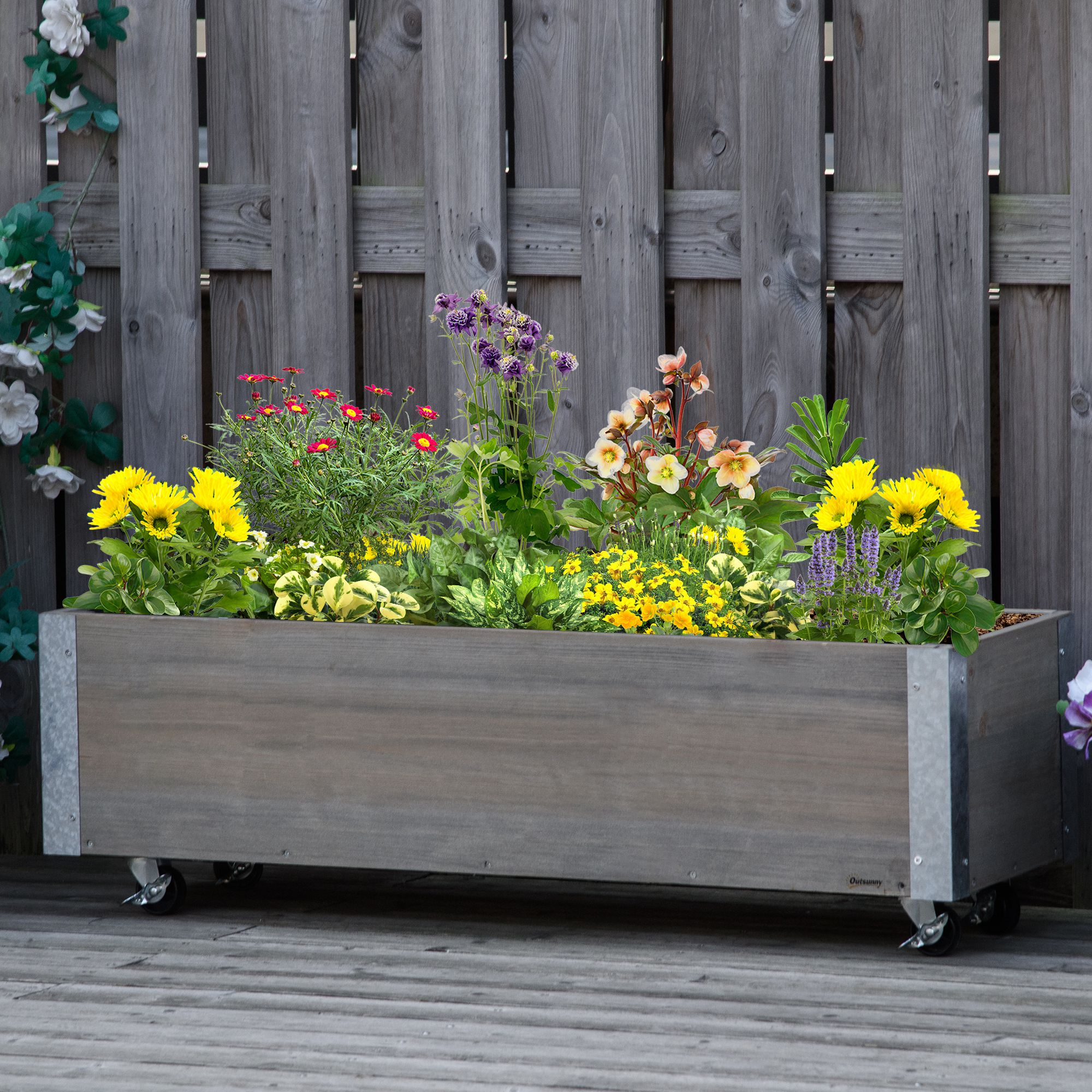 Una fioriera in legno con fiori e piante, su ruote, con una recinzione in legno dietro.