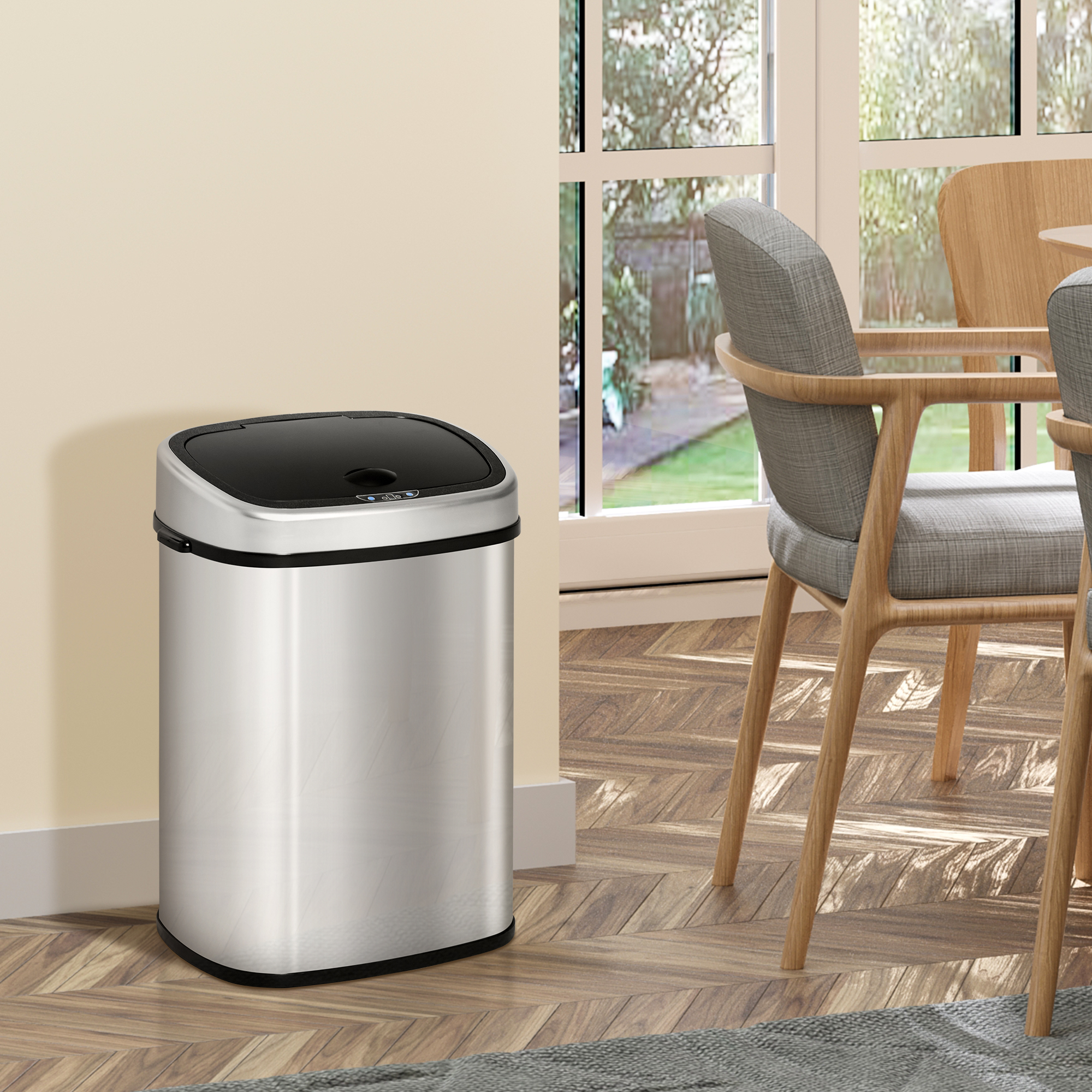 Un cestino automatico in acciaio inossidabile con coperchio nero, all'interno su un pavimento in legno.