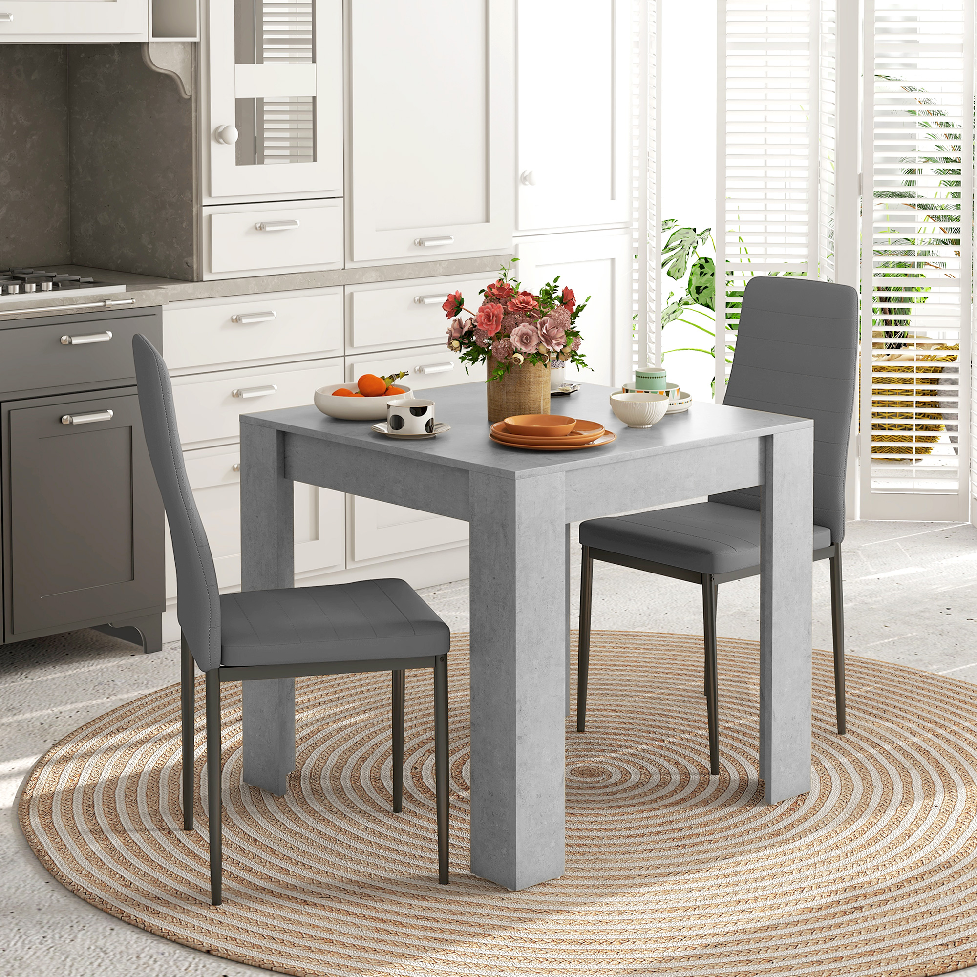 Scena di cucina con tavolo grigio, sedie e fiori su un tappeto fantasia.