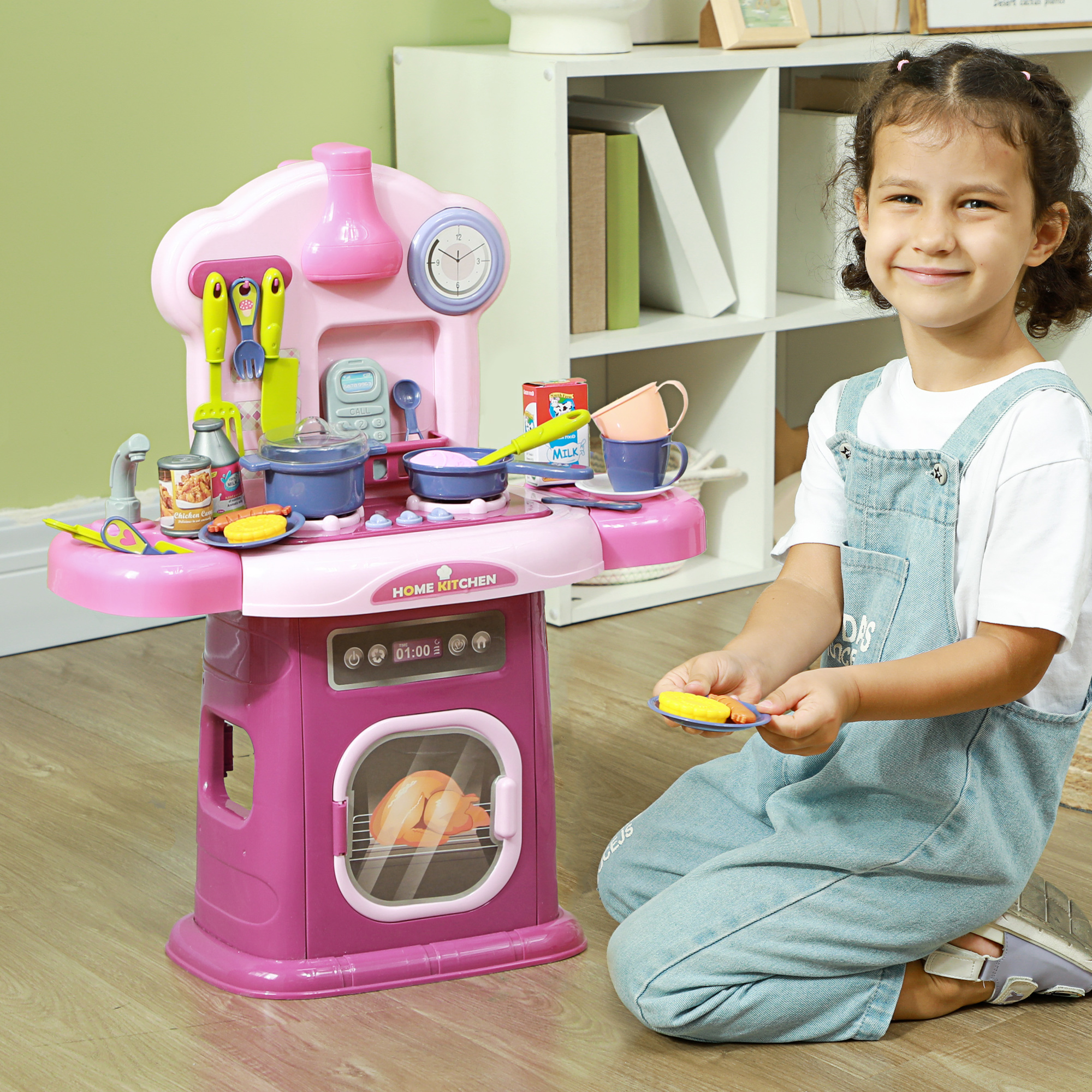 Una bambina seduta vicino a una cucina giocattolo rosa, sorride e tiene un piatto giallo.