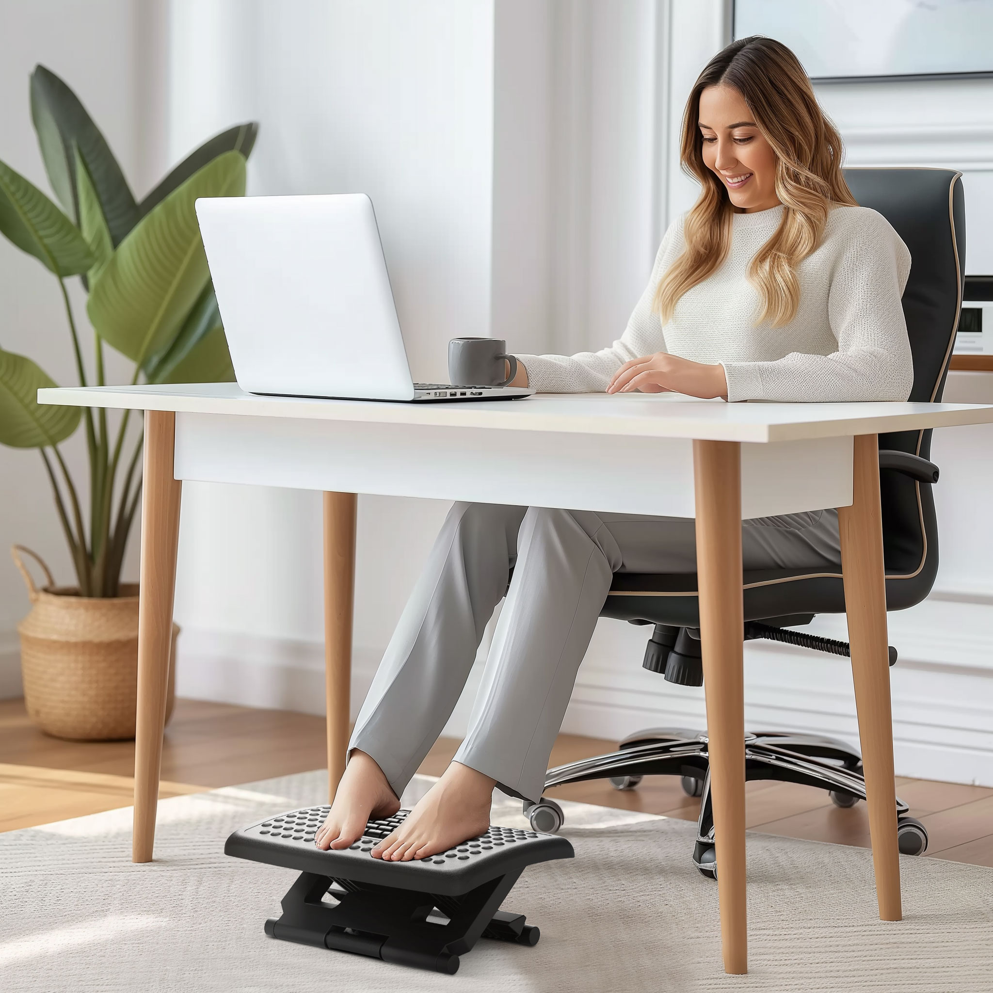 Donna che usa un laptop a una scrivania, piedi su un poggiapiedi. Tazza sulla scrivania.