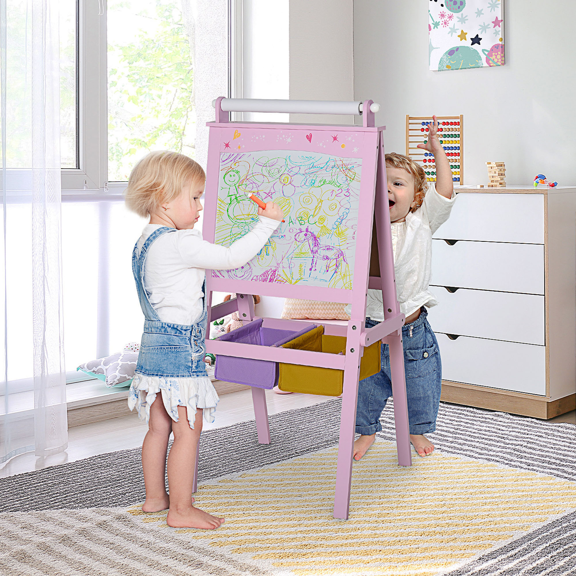 Due bambini che disegnano su un cavalletto rosa. Un bambino tiene un pennarello.
