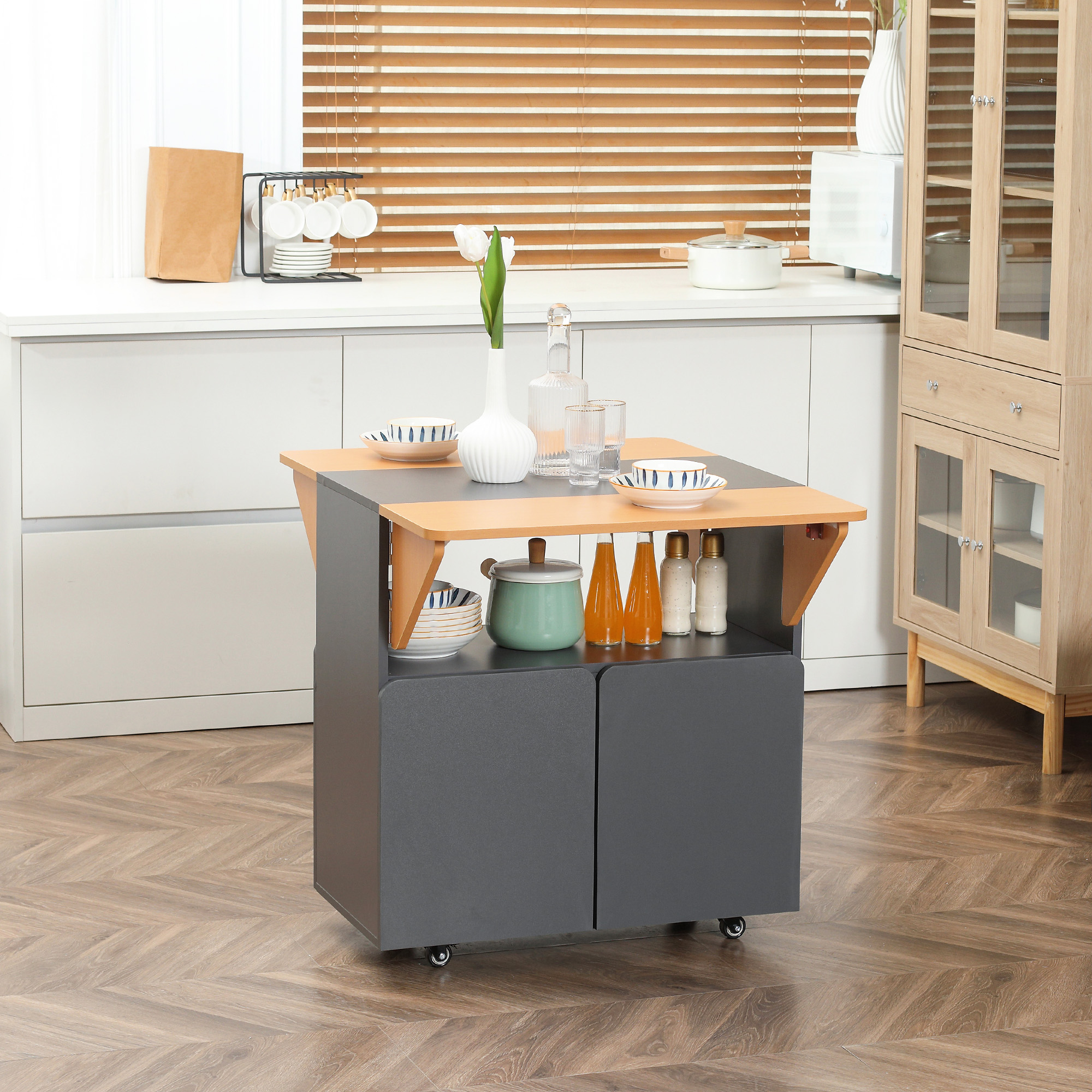 Isola cucina in legno con prolunga tavolo. Ha una base grigia con armadi. La cucina è sullo sfondo.