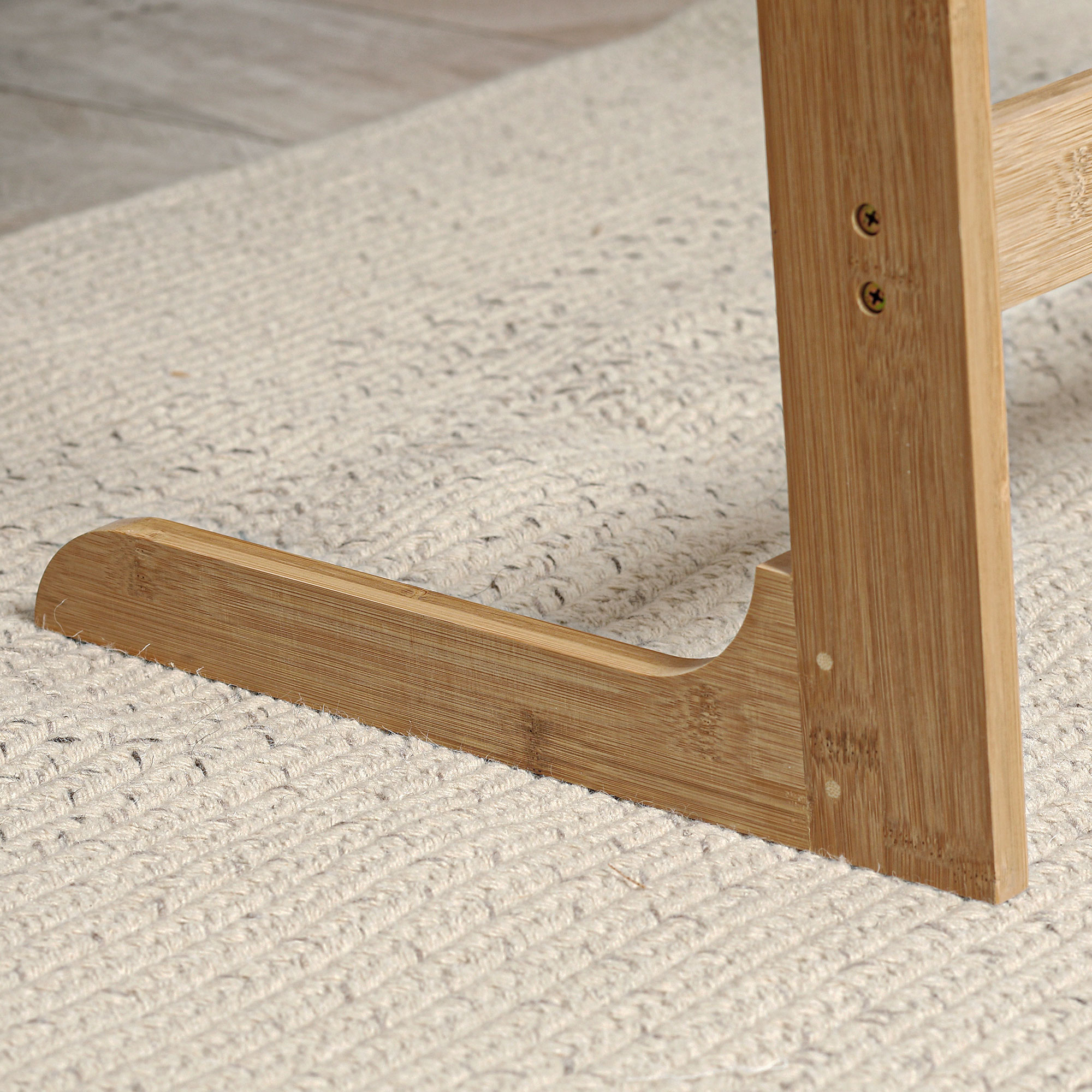 Primo piano di una gamba di sedia in legno su un tappeto chiaro e strutturato. Le viti sono visibili.