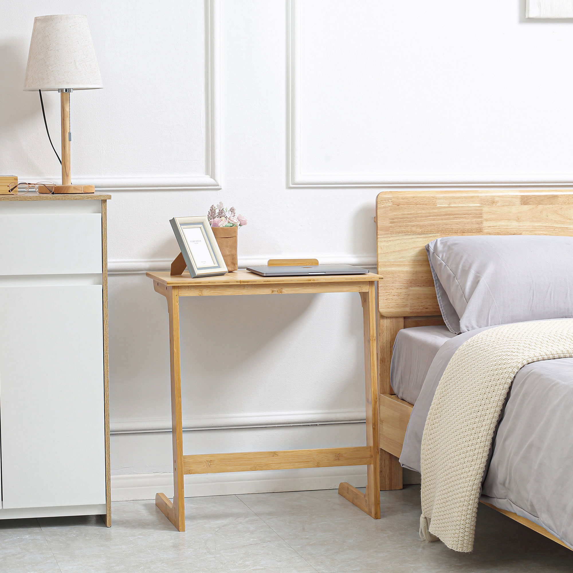 Tavolino in bambù con cornice e laptop. Lampada e letto sullo sfondo.